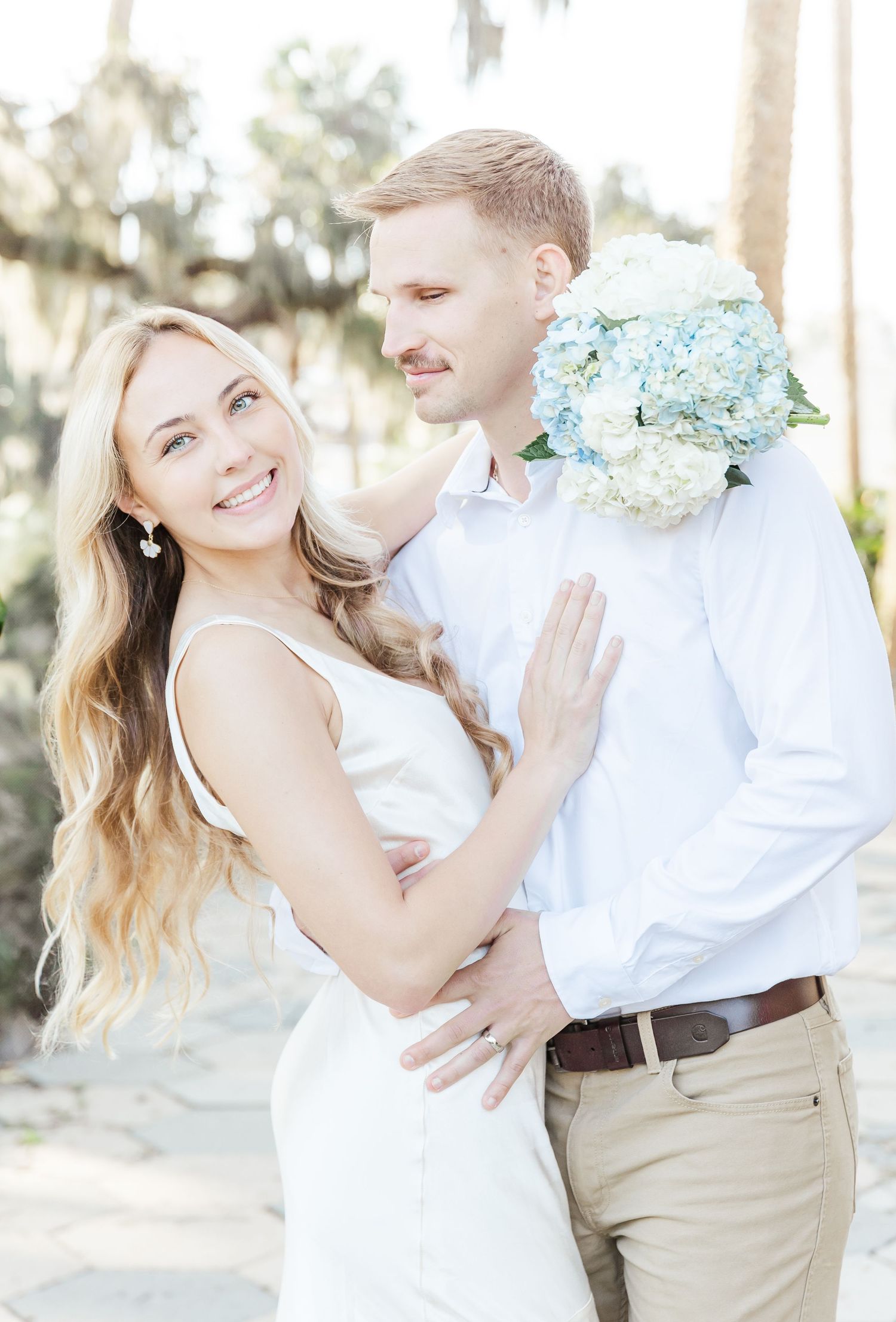 A happy couple shares an intimate moment while holding blue hydrangeas outdoors.