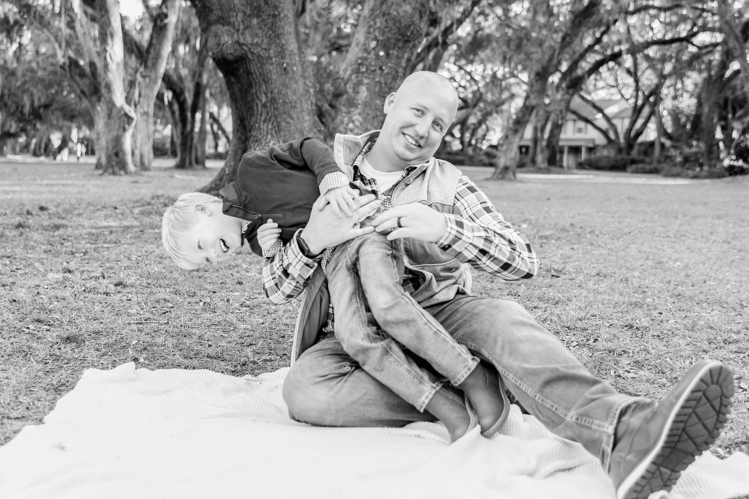 Black and white candid shot of playful family moment on picnic blanket.