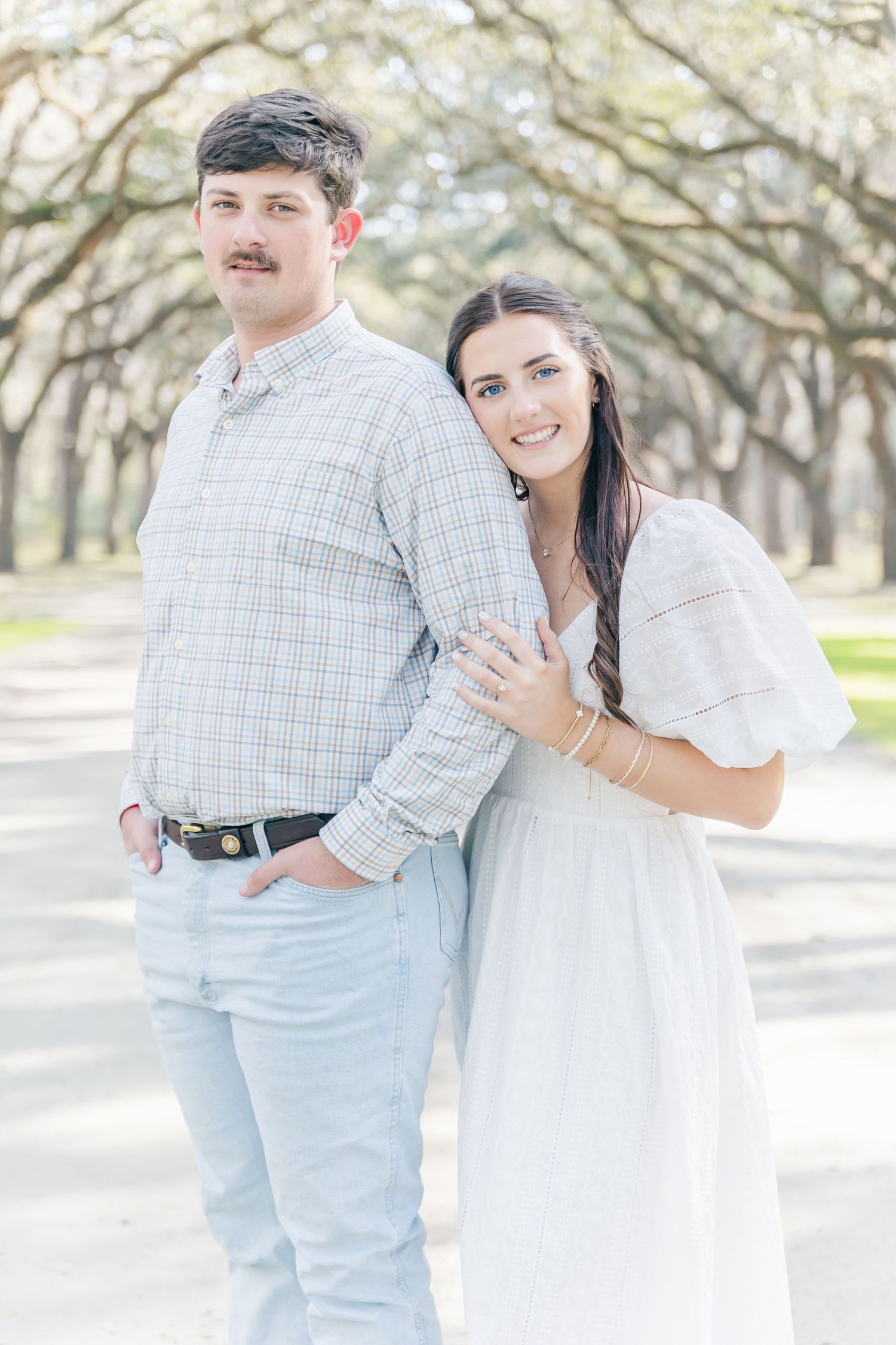A couple shares an intimate moment under an arched canopy of oak trees.