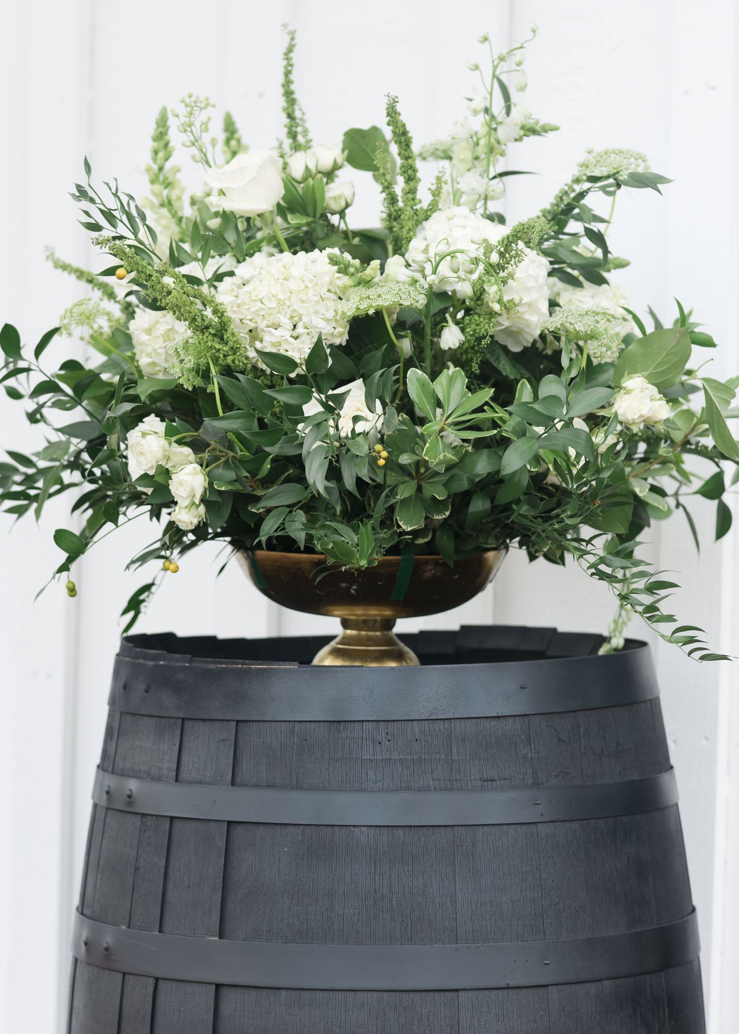 Elegant black wine barrel planters filled with cascading white flowers and lush greenery create a modern garden display.