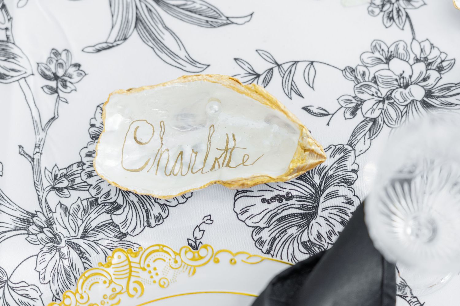 Gold-rimmed oyster shell place card with Charlotte written in calligraphy on floral toile plate.
