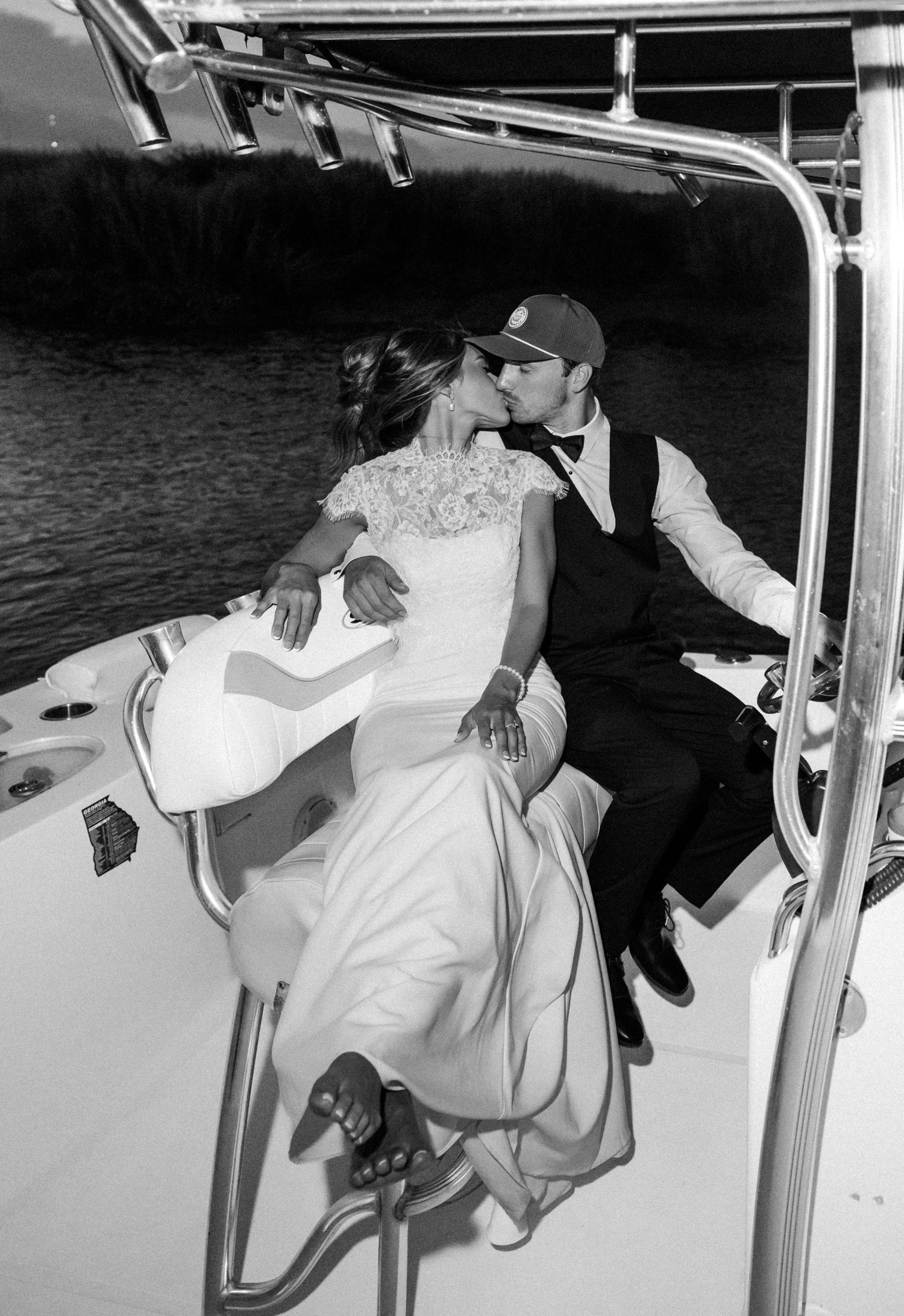 Black and white photo of a bride and groom sharing a kiss on a boat, dressed in wedding attire.