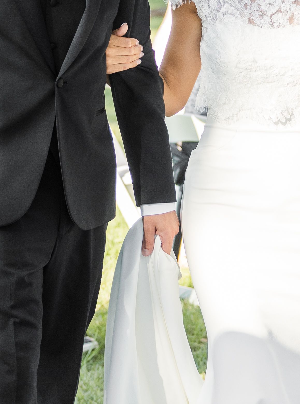 A bride in a white lace gown holds hands with a groom in a black suit during their wedding ceremony.