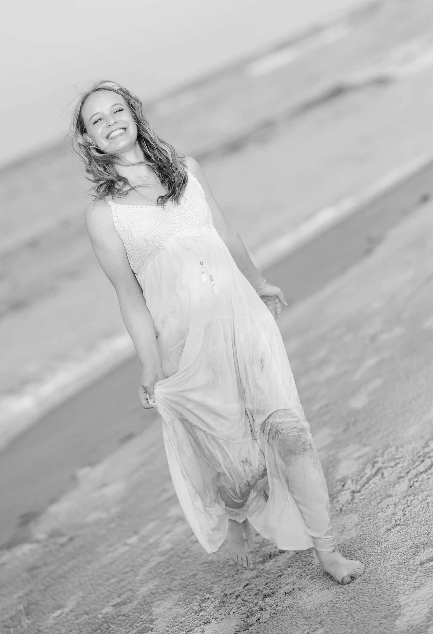 Carefree moment captured on a beach with windswept hair and white flowing dress.