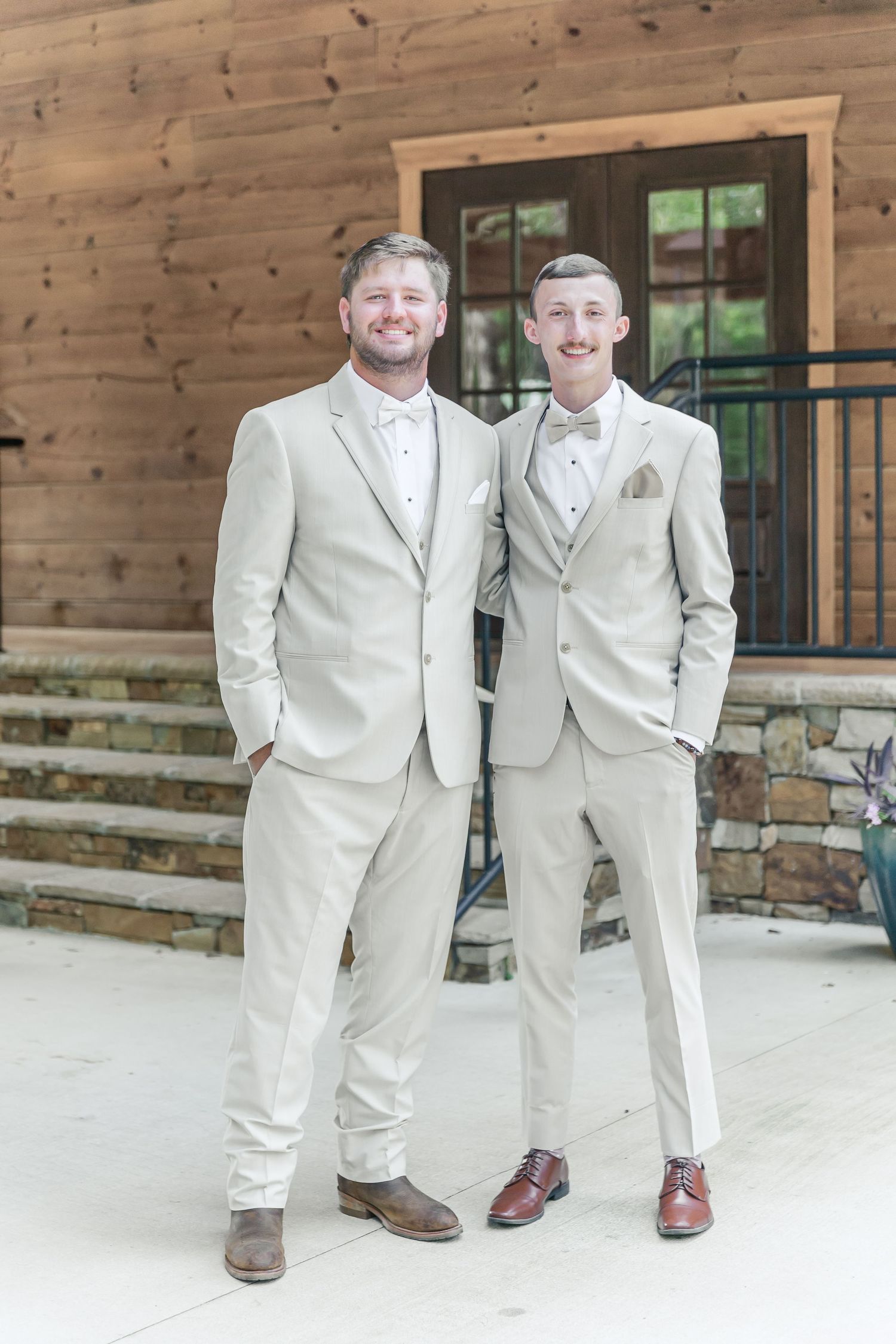 Two people in matching light suits share a happy moment outside a rustic building.