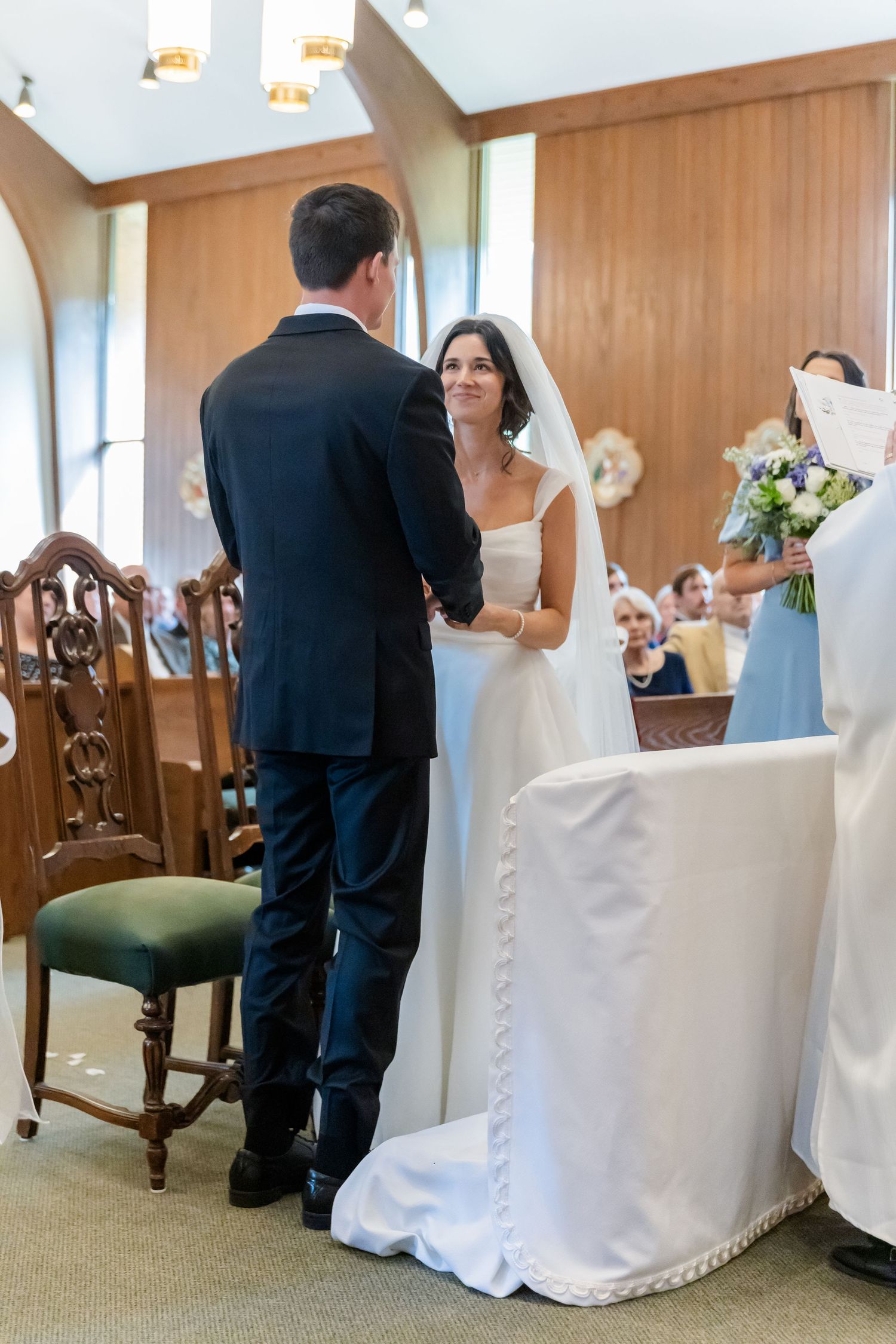 Wedding reception setup in an elegant room with white chair covers and wooden paneled walls.