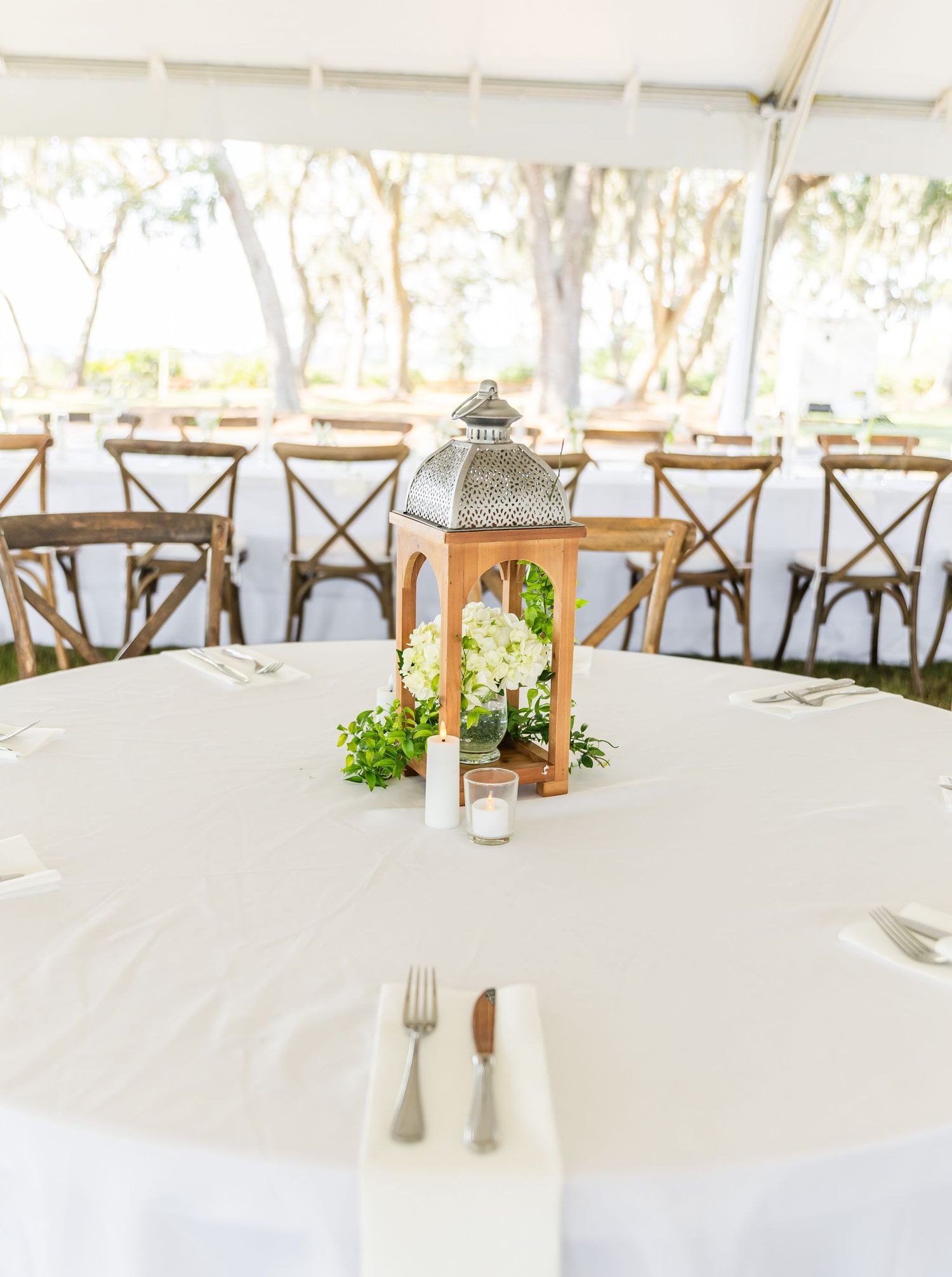 Elegant wedding reception table setup with white linens, wooden cross-back chairs, and delicate floral centerpieces.