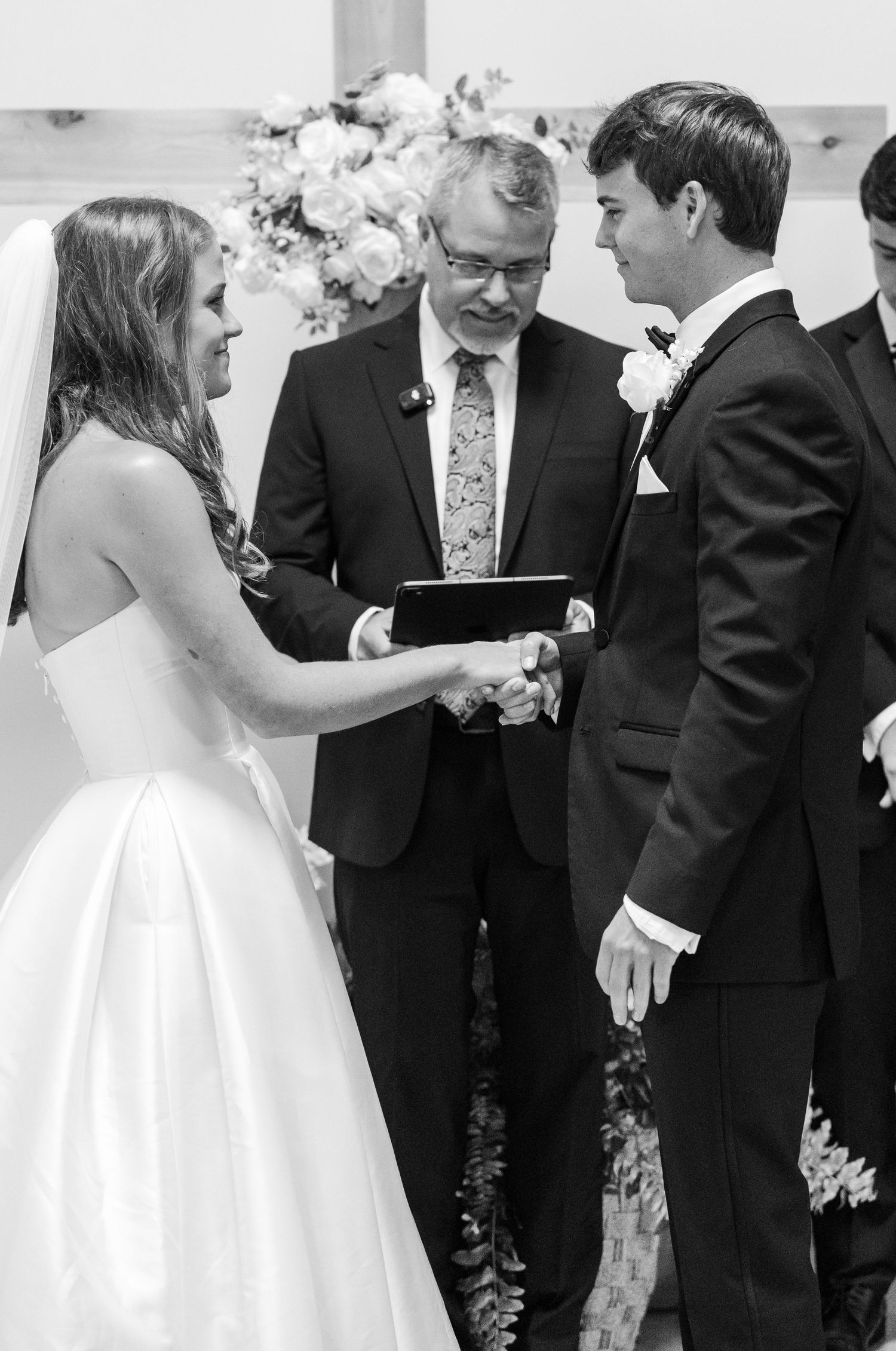 Bride and groom exchange vows at wedding altar with officiant holding book during black and white ceremony.