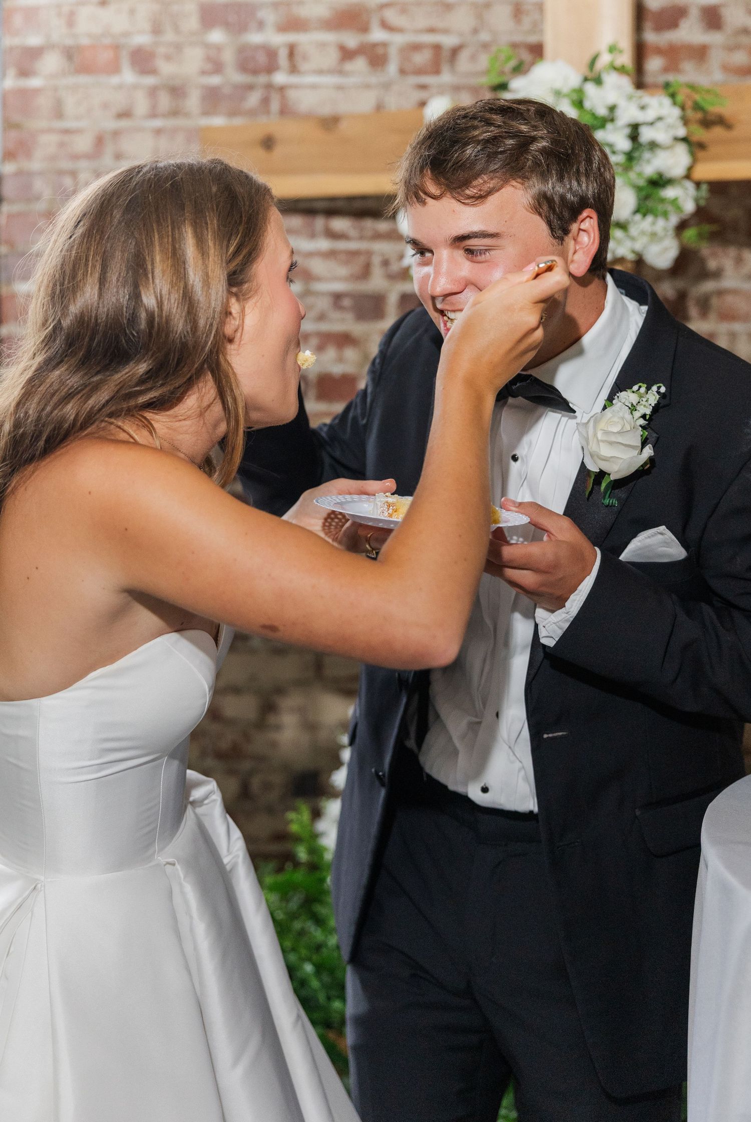 Bride playfully smashes wedding cake on grooms face during cake cutting ceremony.