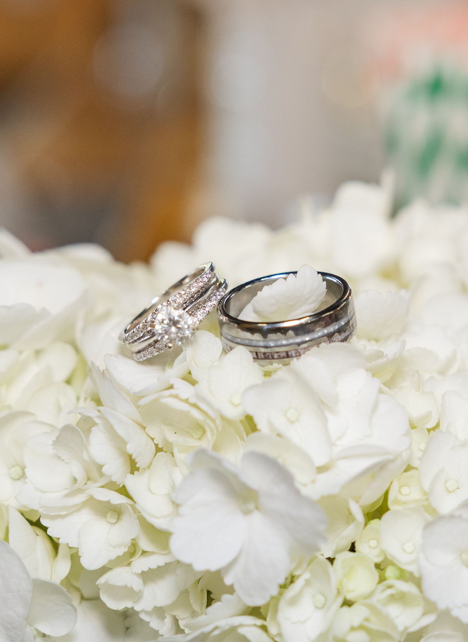 Wedding rings displayed on white hydrangeas, featuring diamond engagement ring and antler-engraved band.