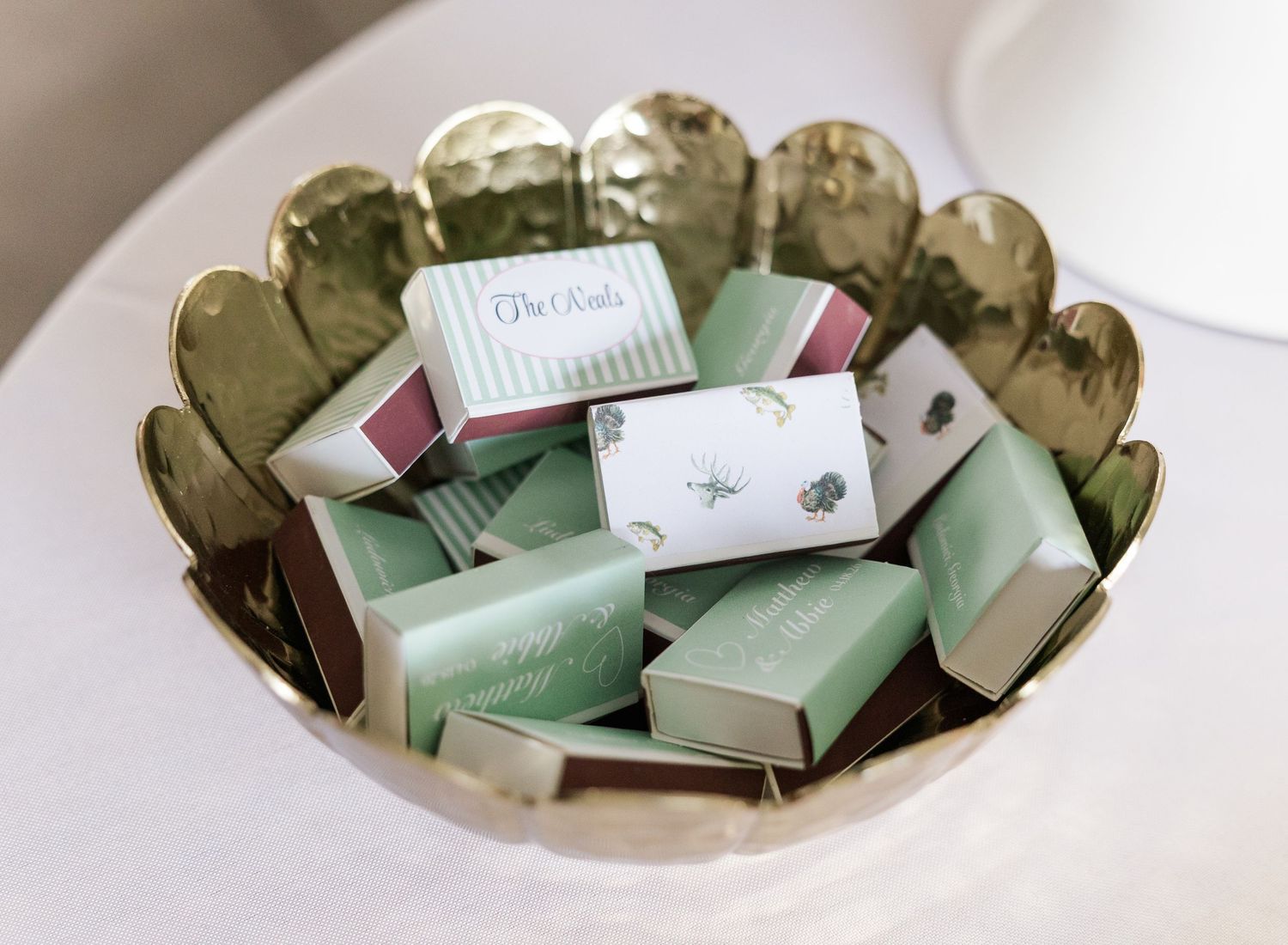 Gold scalloped bowl filled with mint green wedding favor boxes tied with ribbon on white table.