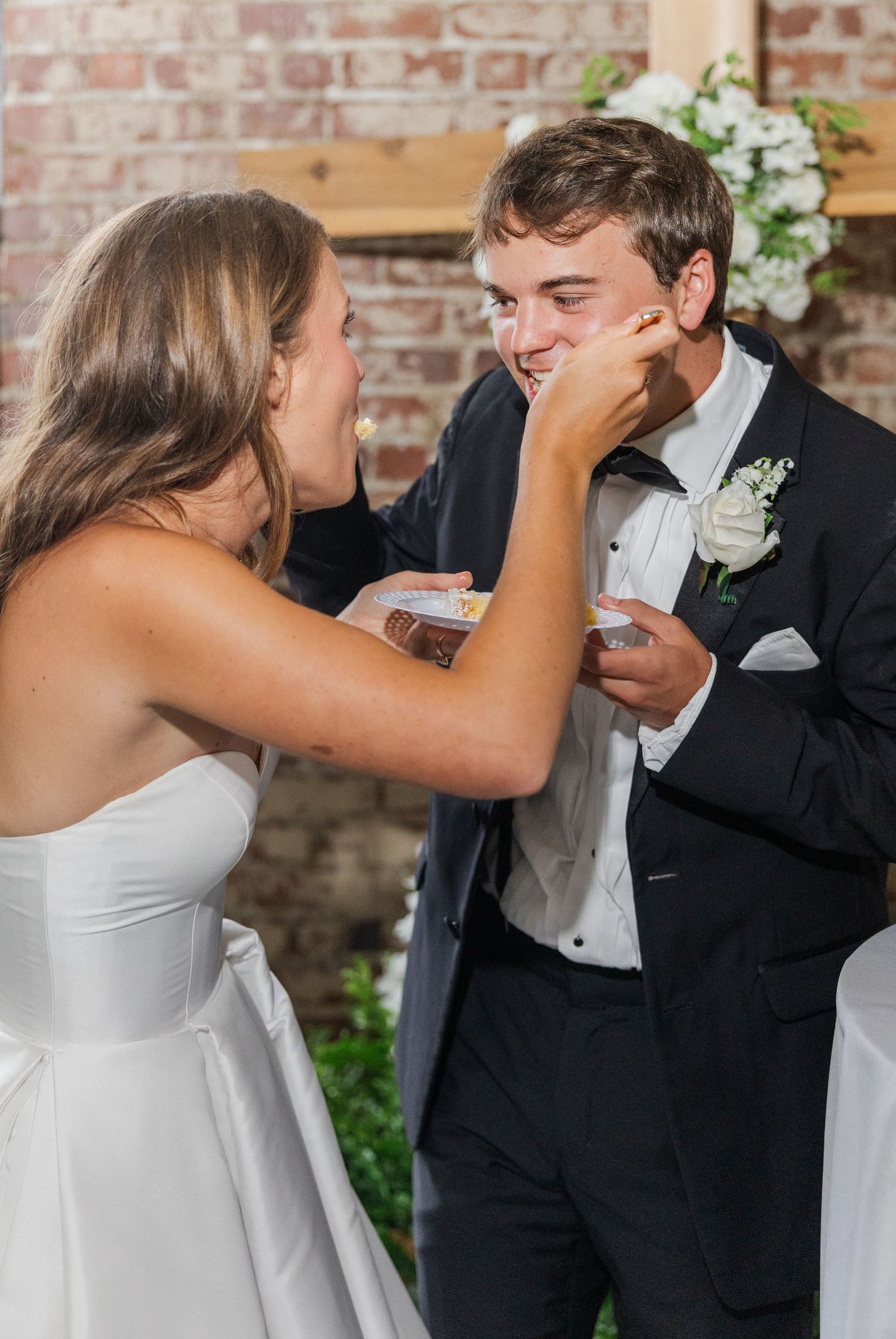 Bride playfully smashes wedding cake on grooms face during fun reception cake cutting moment.