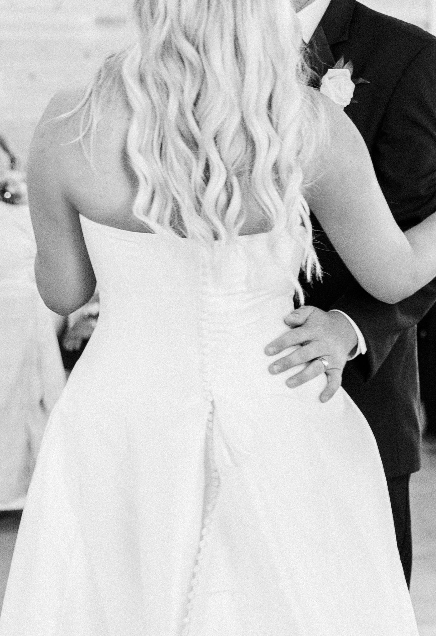 Black and white photo of bride in strapless gown with long wavy hair dancing with groom in dark suit.