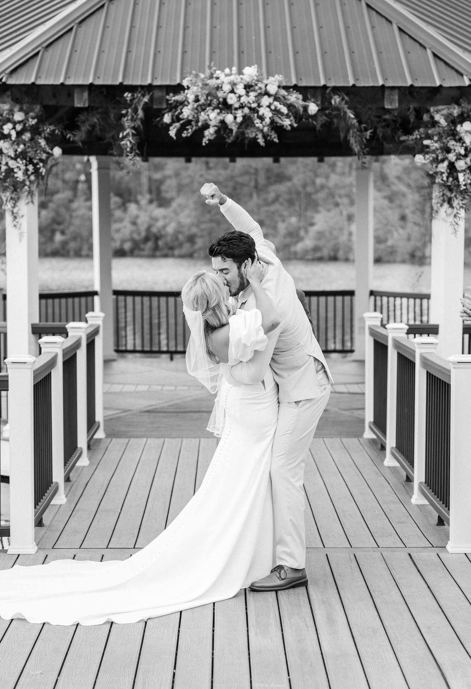 Black and white photo of groom dipping bride for kiss under floral gazebo at wedding.