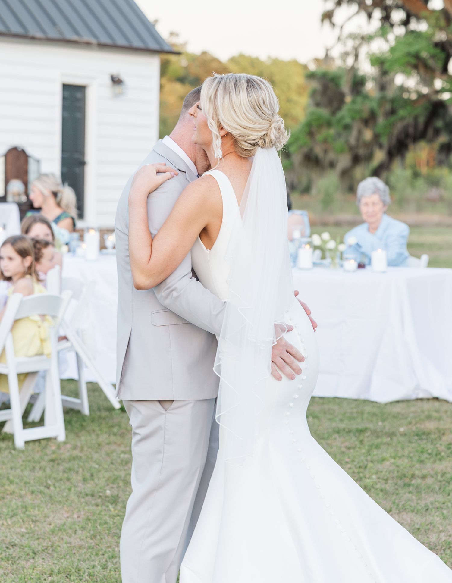 Bride and groom sharing first dance kiss outdoors at evening wedding reception on green lawn.