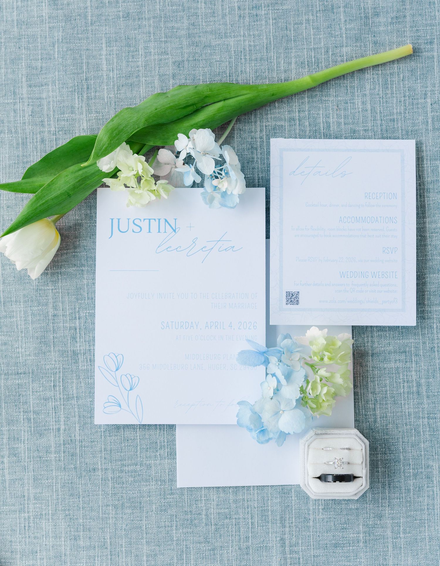 Blue and white wedding invitation suite with tulip, hydrangeas, and diamond ring box on linen background.