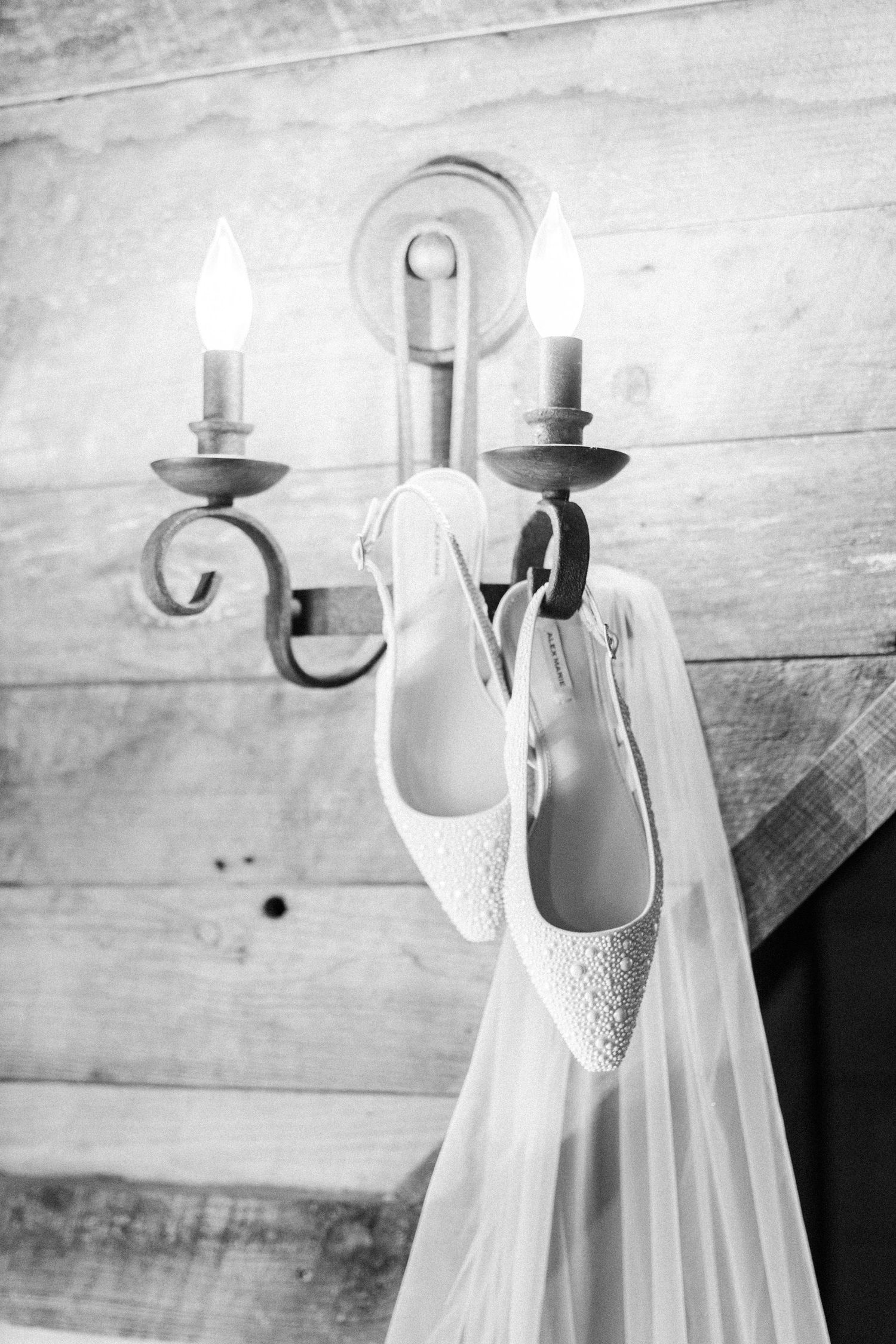Bridal heels and veil hanging on a rustic candle wall sconce in black and white.