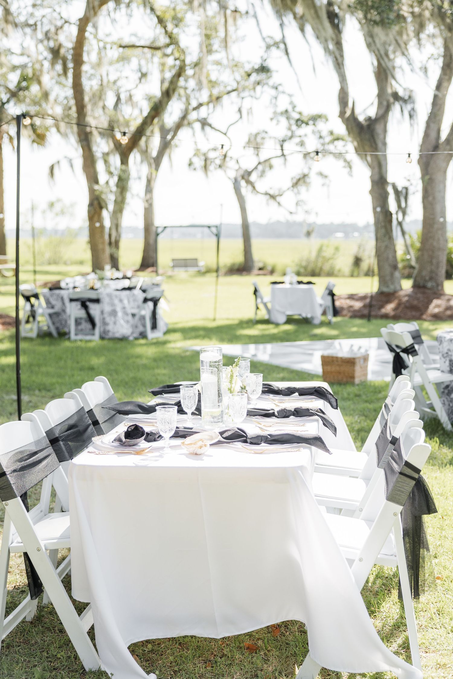 Elegant outdoor wedding reception tables with black and white decor under Spanish moss trees.
