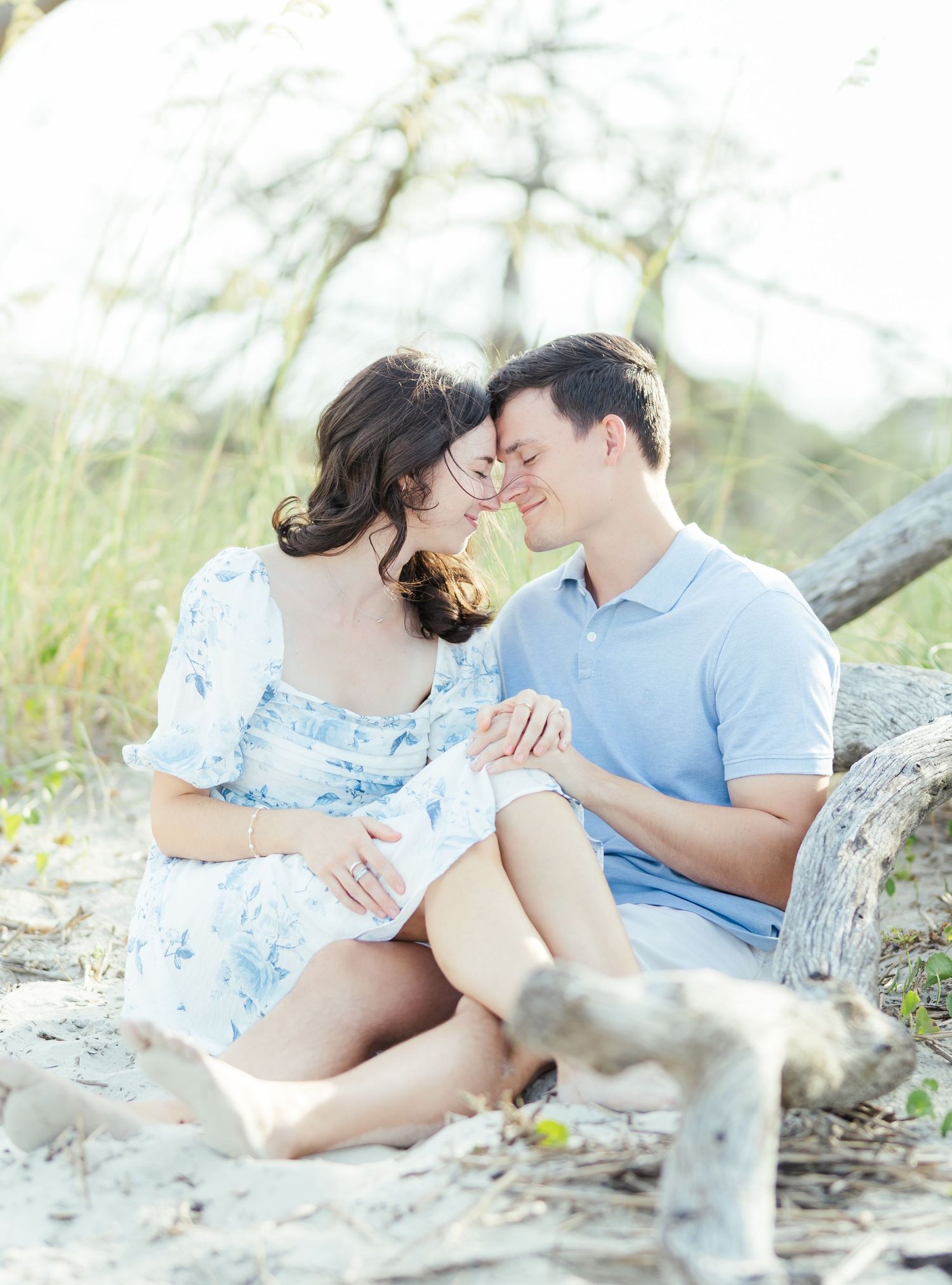 A romantic beachside moment captured among driftwood and sea grass in soft lighting.