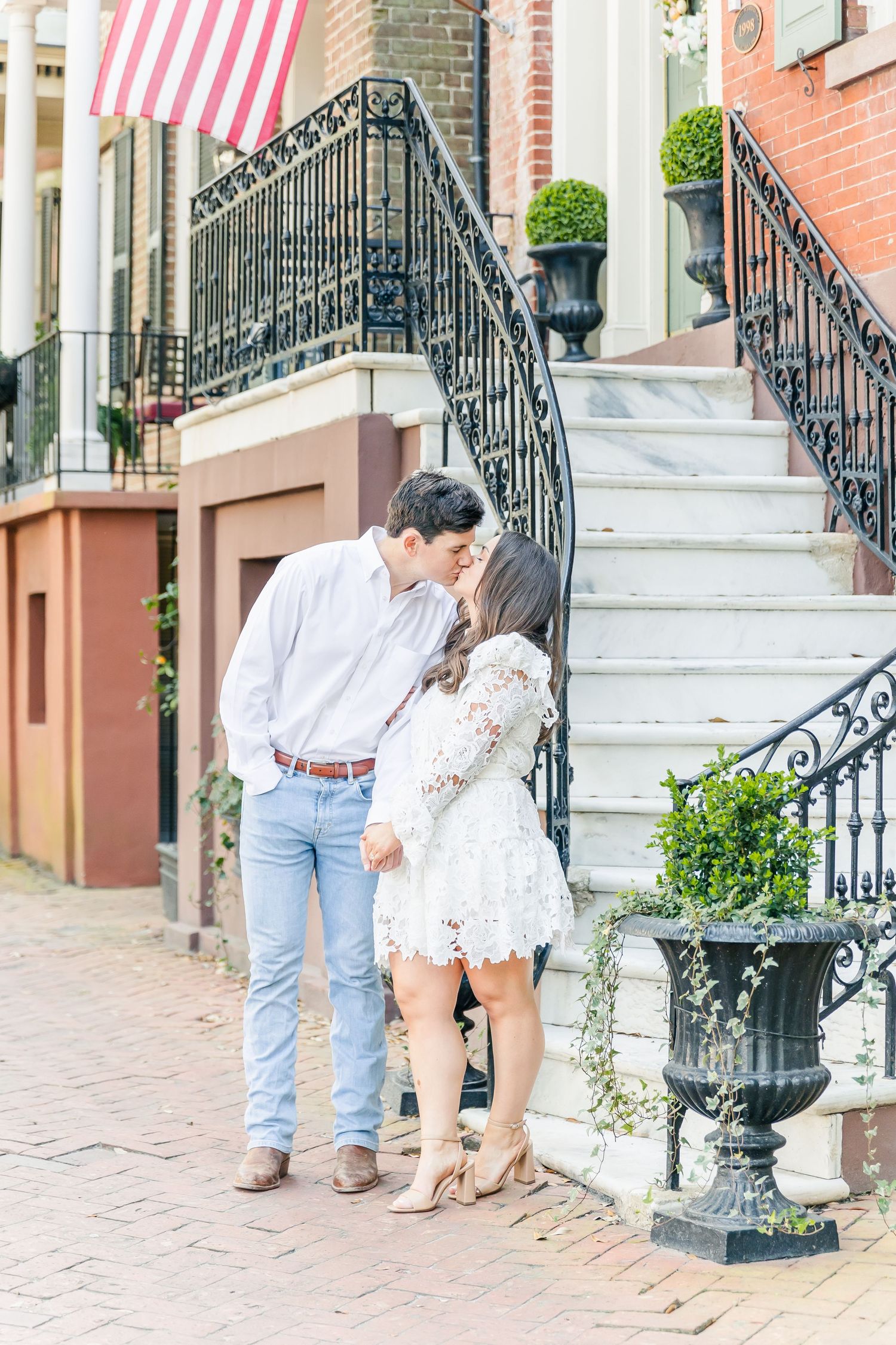 Romantic couple enjoying a tender moment on brick steps with an American flag flying above.