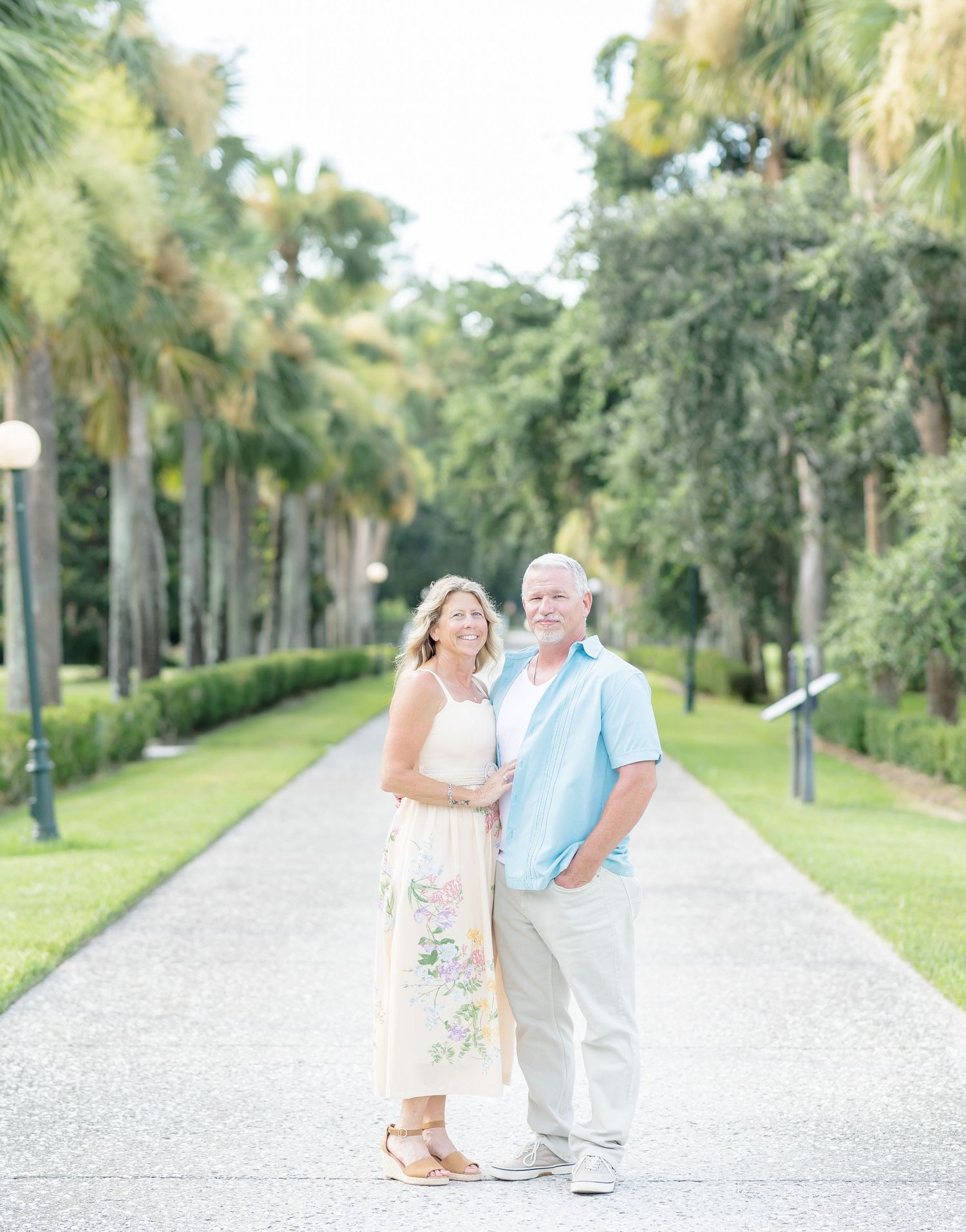 A couple shares tender moments on a palm tree-lined pathway in a romantic outdoor photoshoot.
