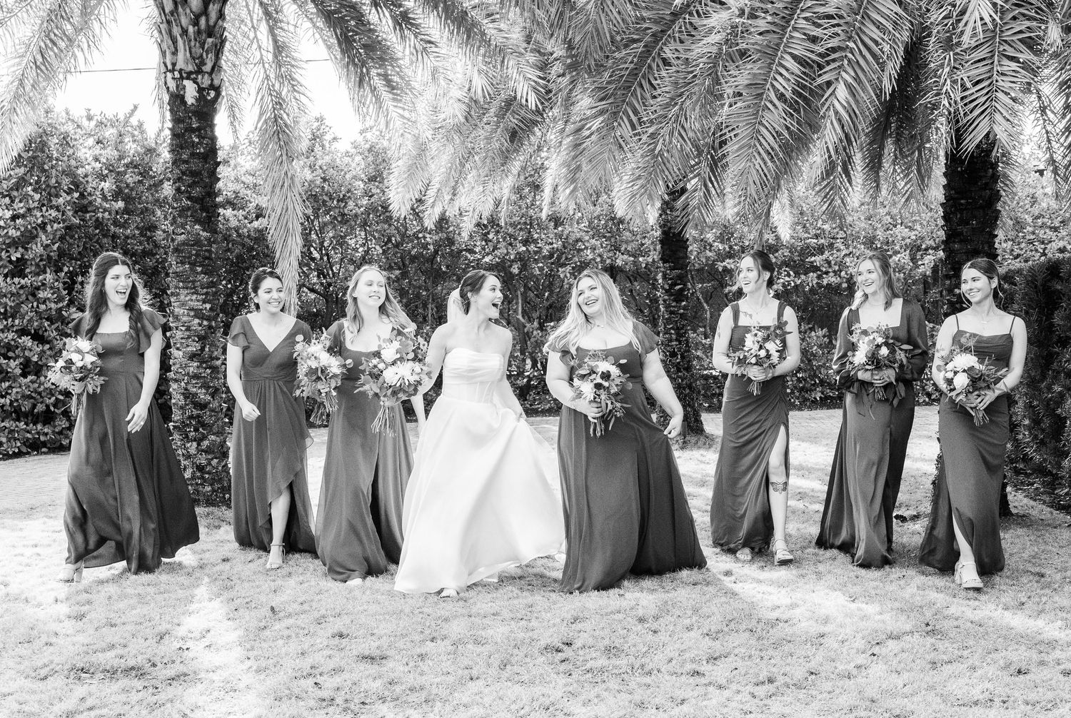 Wedding party group photos taken outdoors under palm trees in black and white.