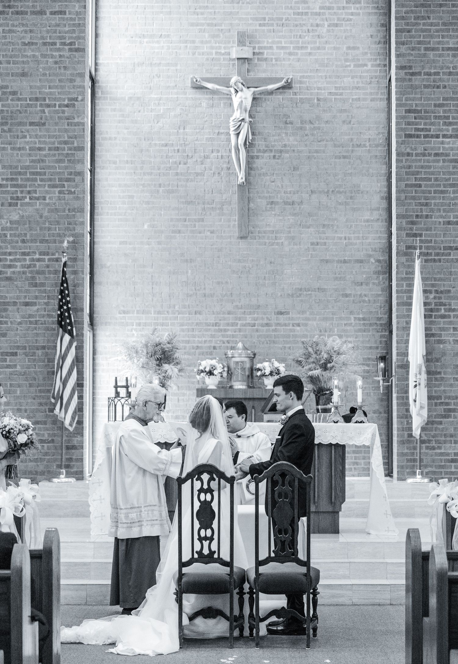 Black and white photo of church wedding ceremony with crucifix and brick wall backdrop.