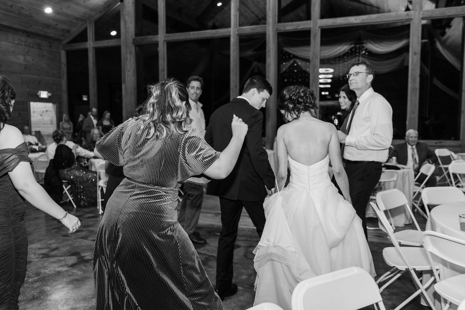 Wedding reception guests dancing and celebrating in a wooden barn venue with white decor.