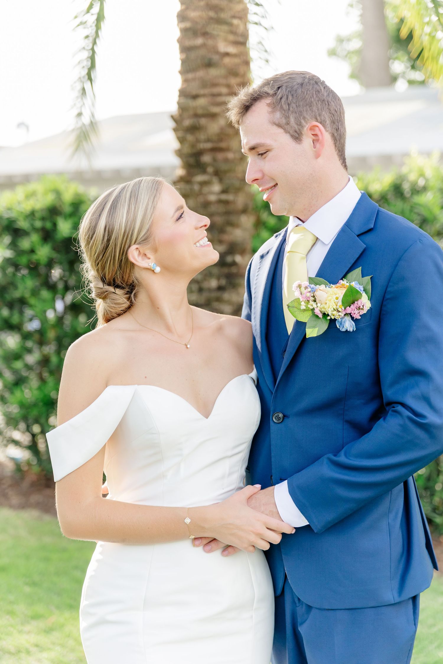 A couple shares candid laughs during their outdoor wedding photos beneath swaying palm trees.
