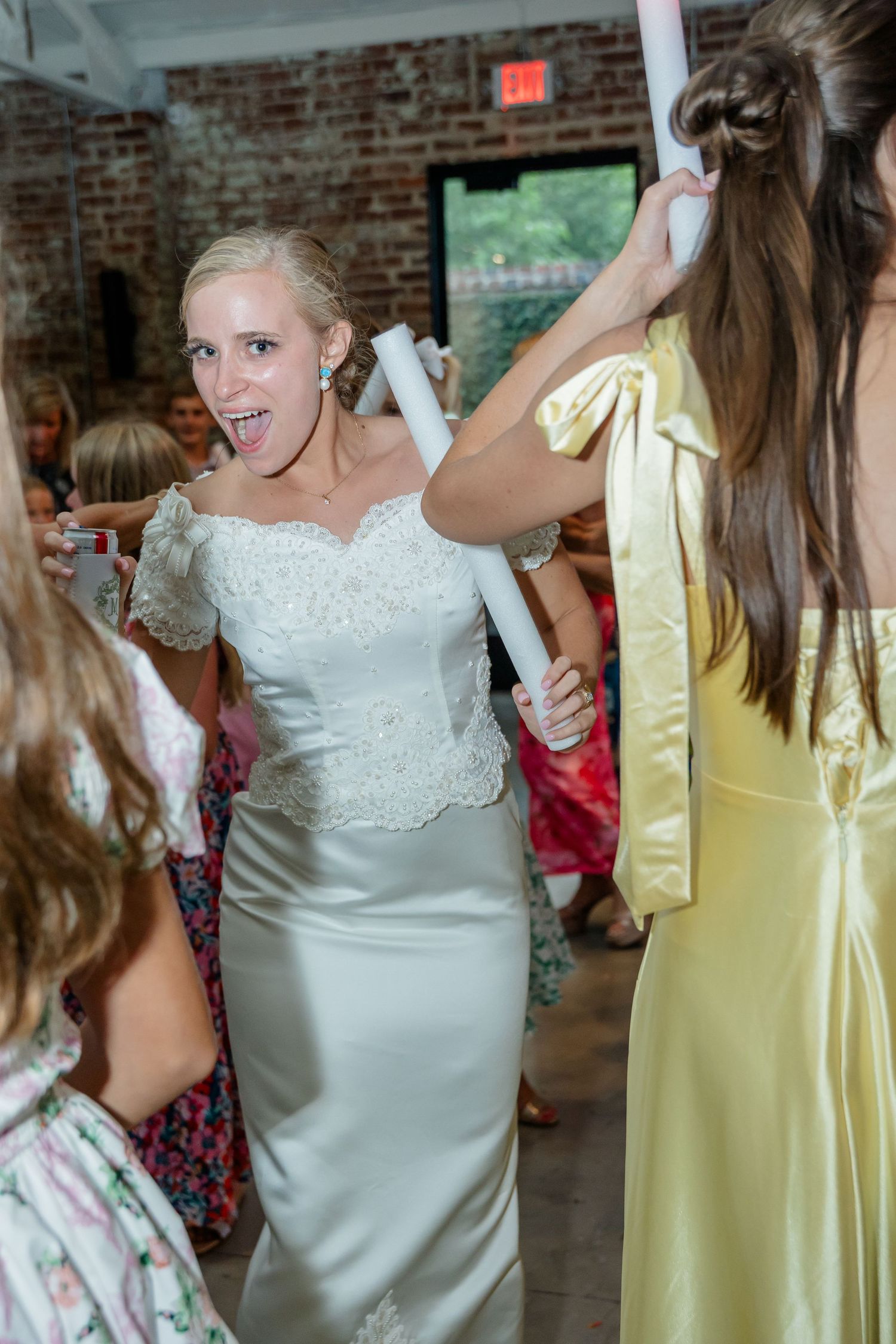 Wedding party members dancing with illuminated foam batons at an indoor reception.