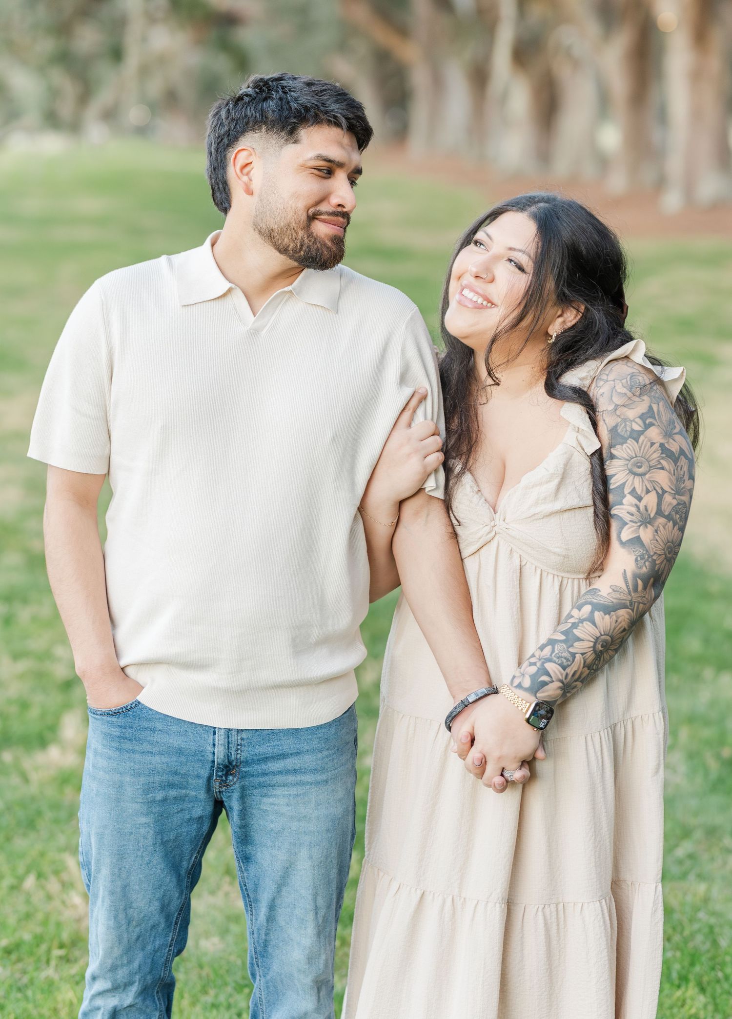 A couple in casual attire shares intimate moments during an outdoor photoshoot in a grassy park setting.