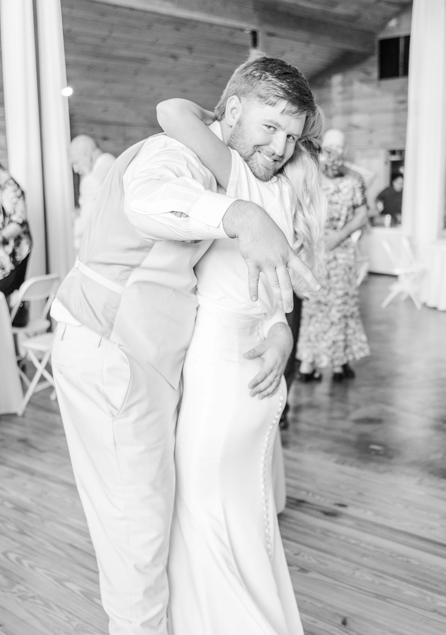 Sweet monochrome moment of newlyweds dancing together in a rustic reception venue.