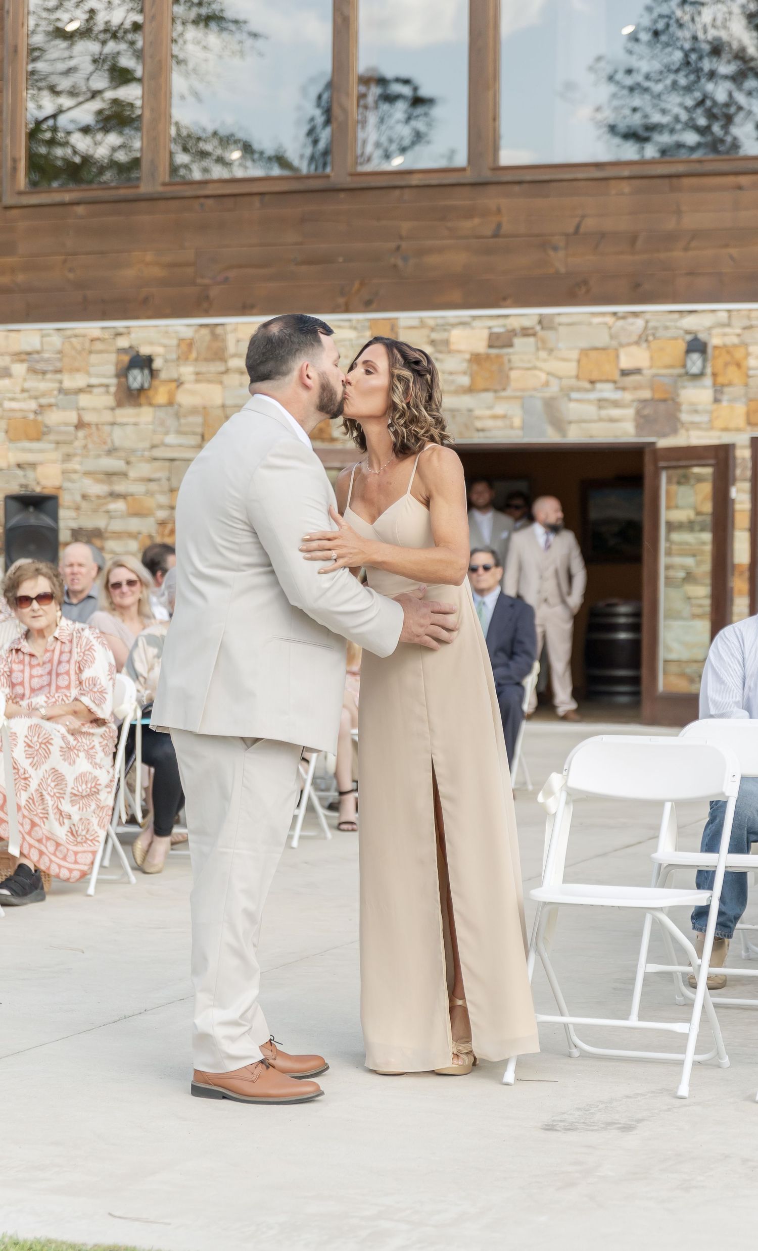 A couple shares an intimate moment during their wedding ceremony in front of a stone building.