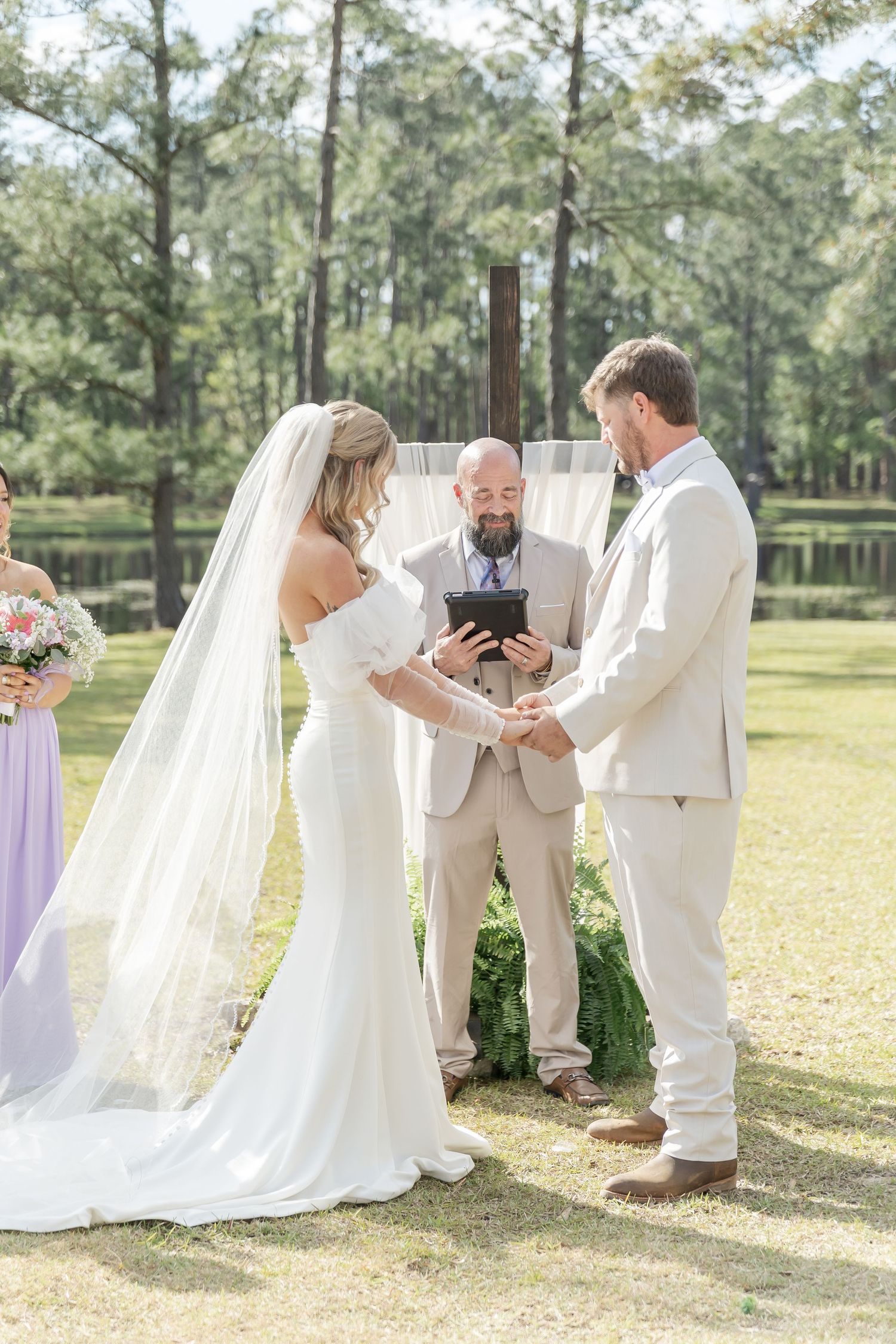An intimate outdoor wedding ceremony taking place on a sunny day with pine trees in the background.