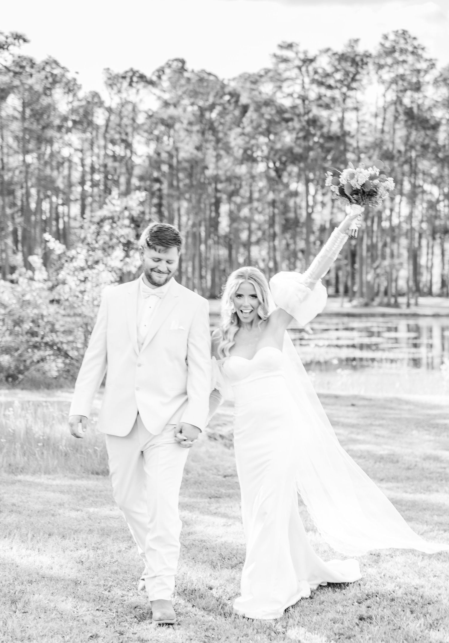 Black and white photo of newlyweds celebrating with bride raising bouquet in joyful pose.