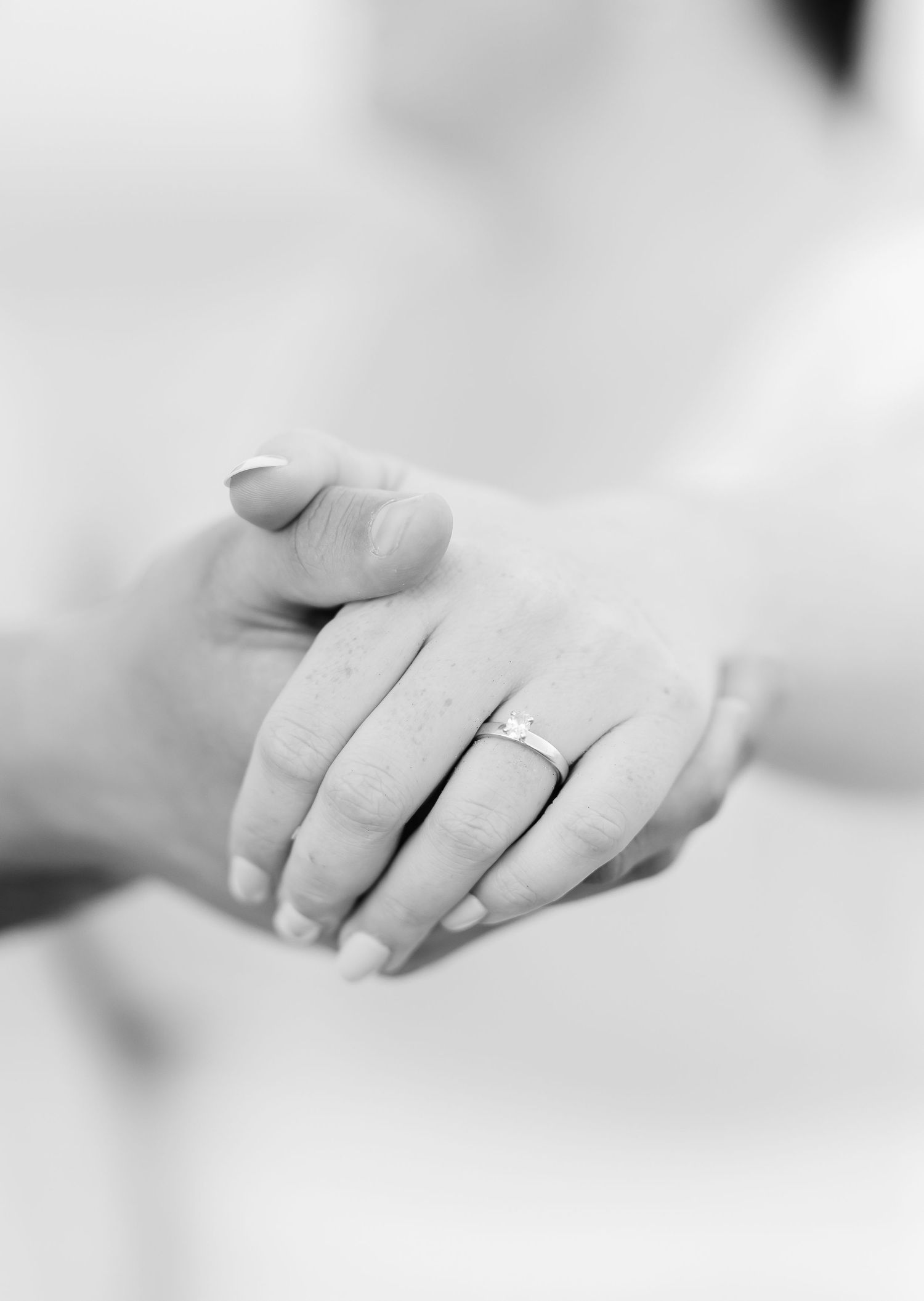 A black and white close-up of hands with an engagement ring.