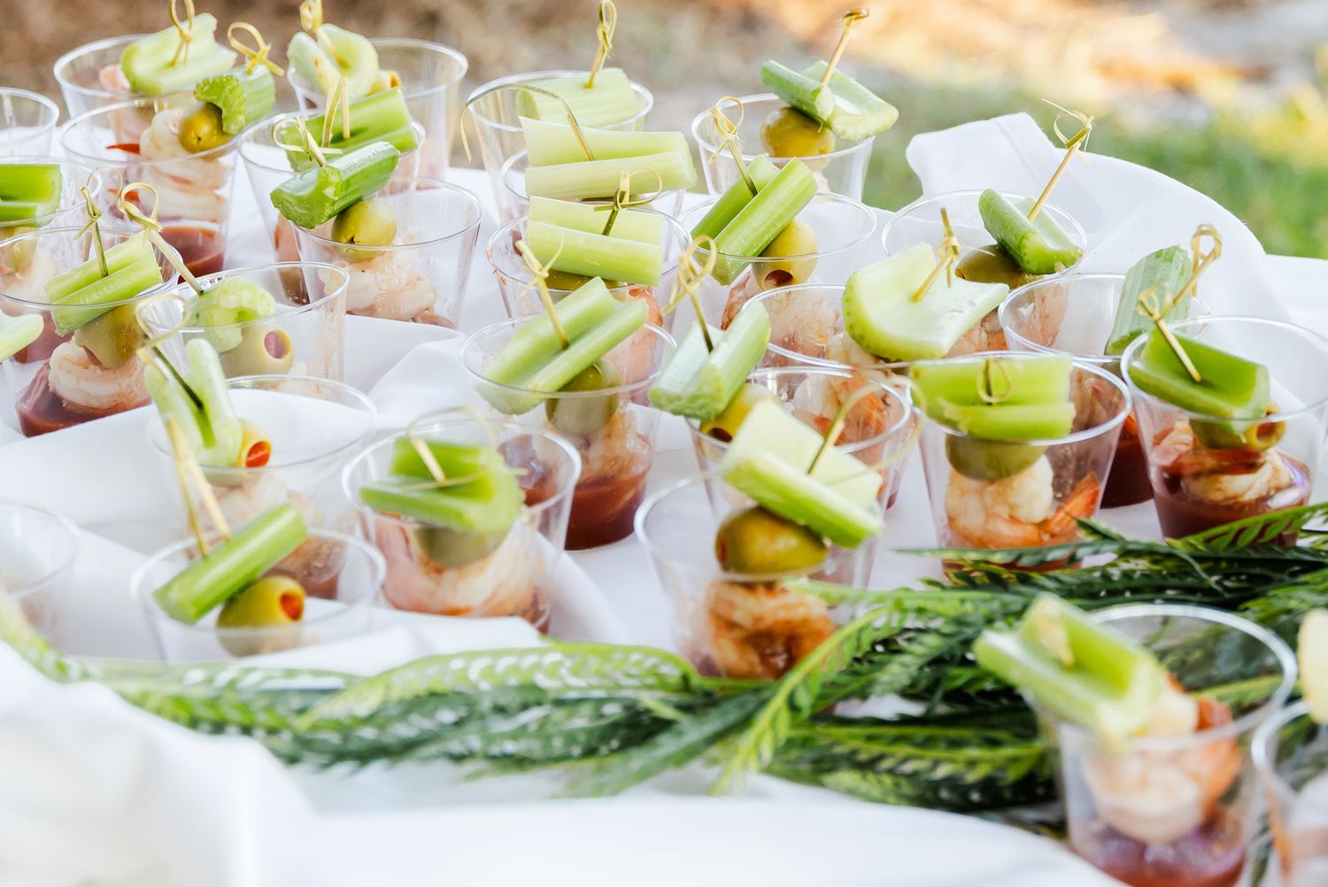 Elegant appetizer shooters garnished with celery and shrimp on white tablecloth.