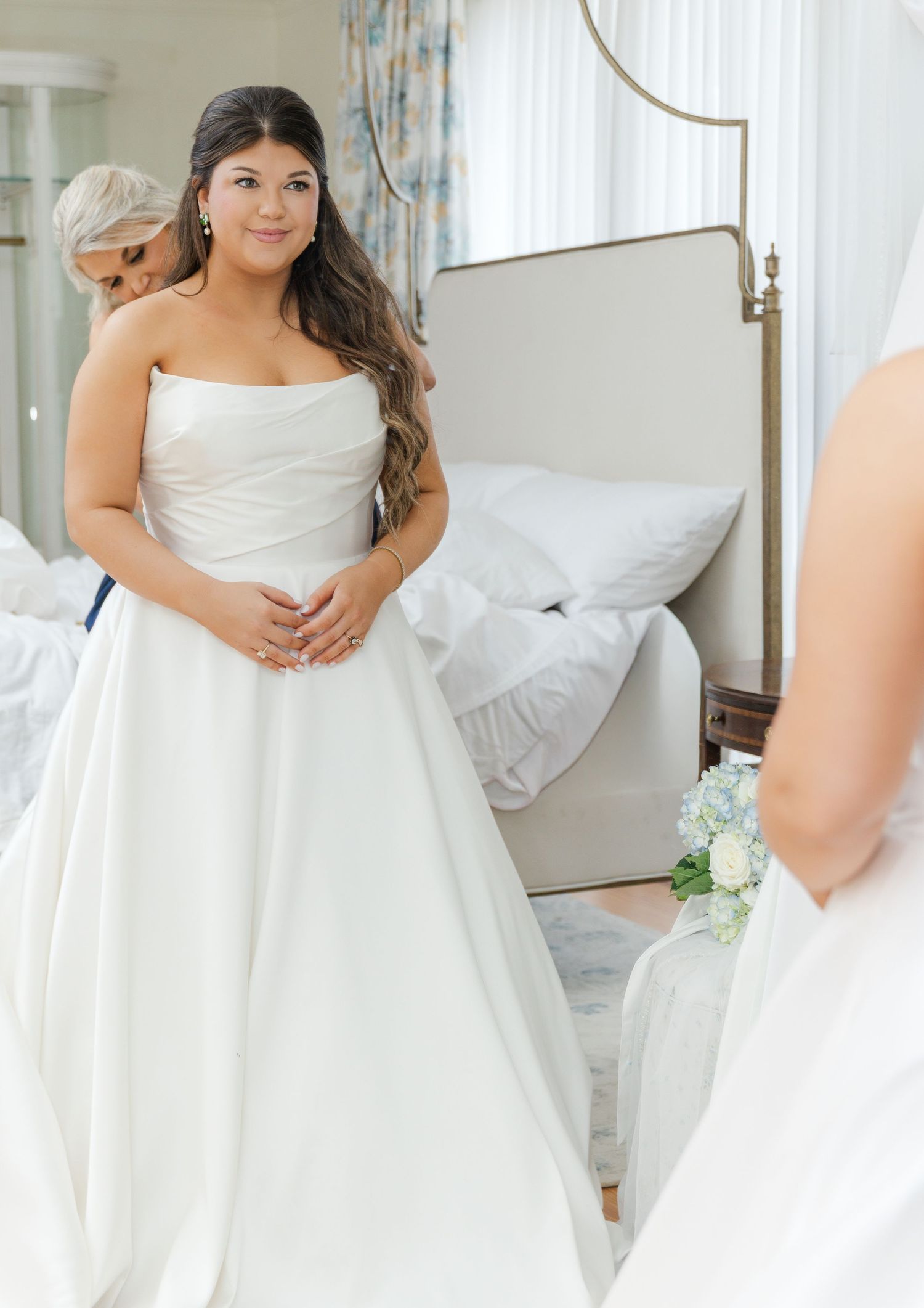 Bride in strapless white ball gown admiring her reflection in a large mirror before her wedding ceremony.