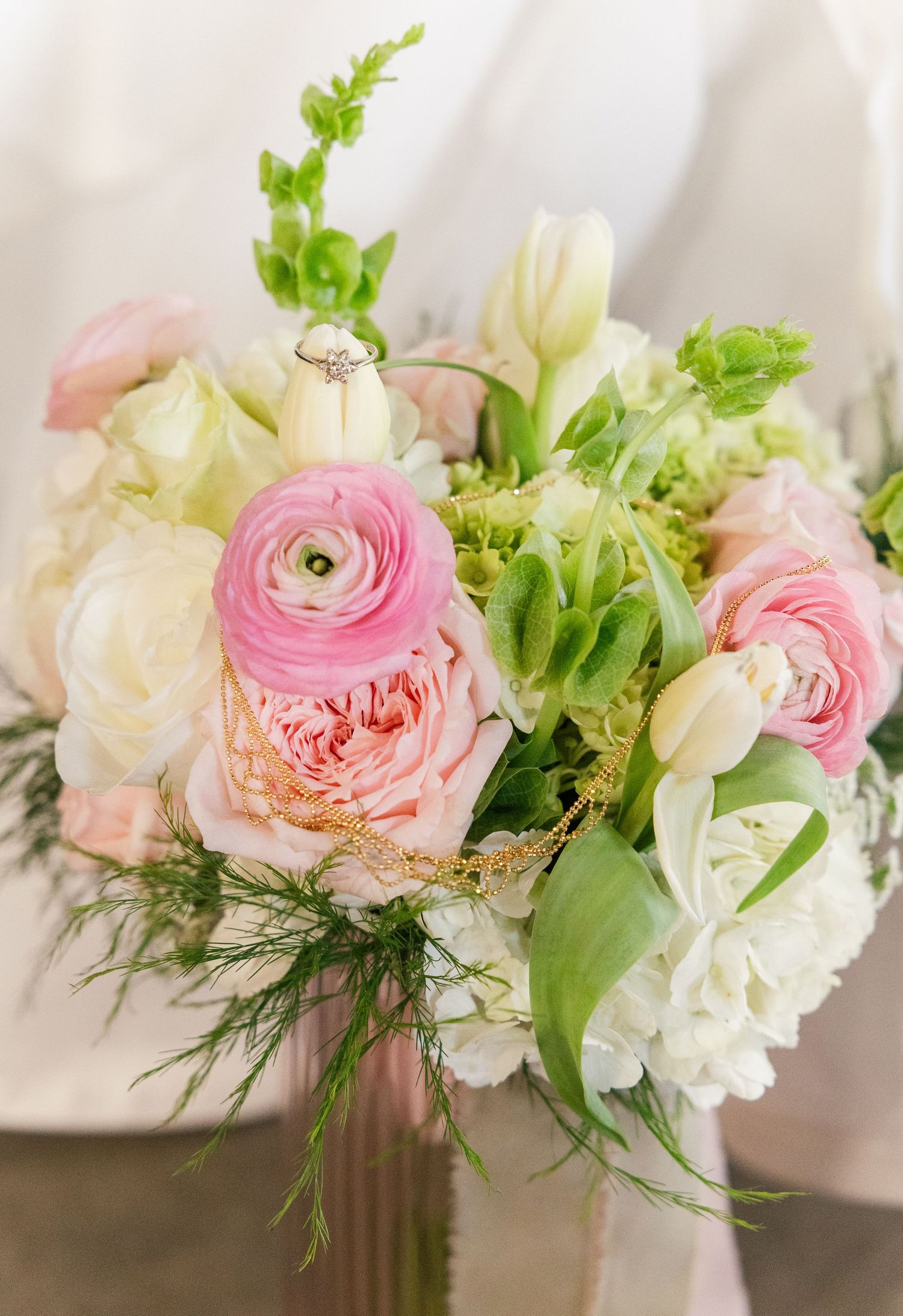 Romantic bridal bouquet featuring pink ranunculus, roses, white tulips, hyacinths, and greenery with a diamond engagement ring.