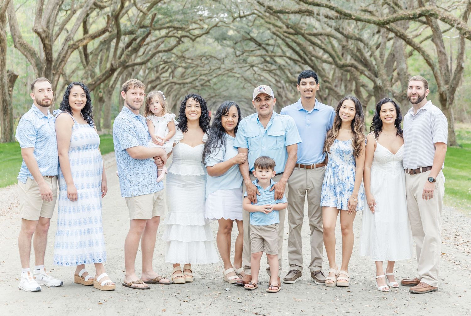 Large group in coordinating blue and white outfits poses together on tree-lined path.