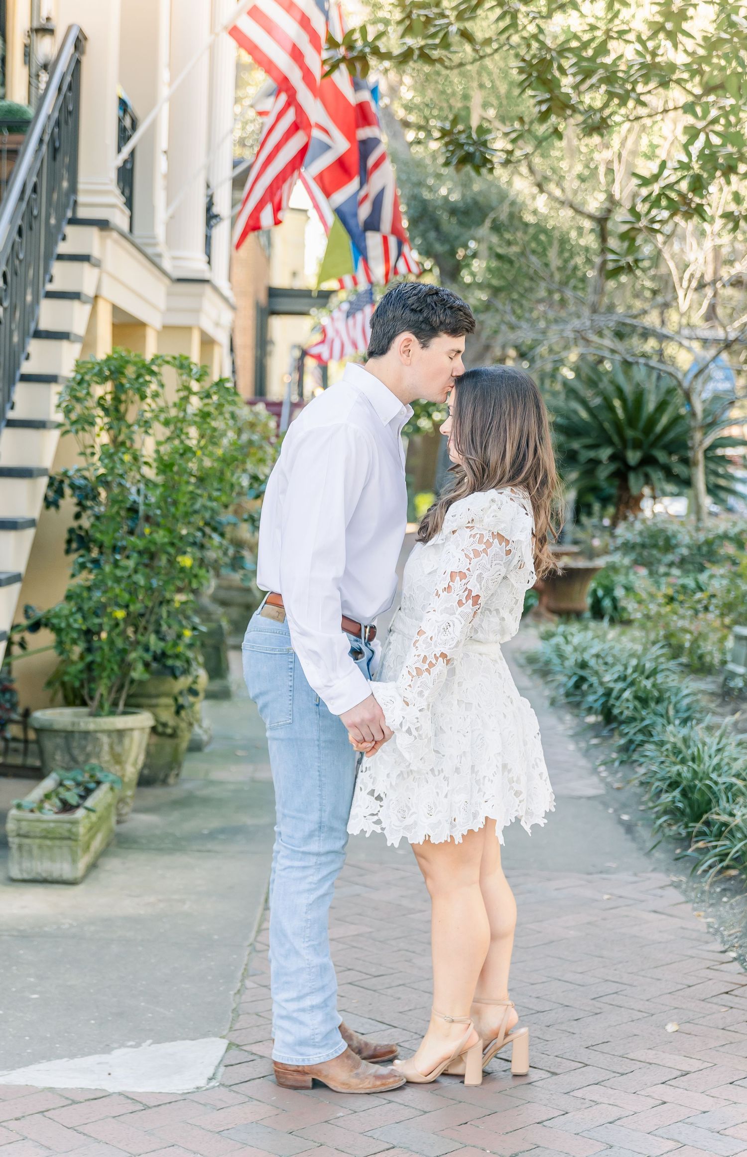 Romantic couple in white outfits sharing an intimate moment on a charming brick pathway with American flags.