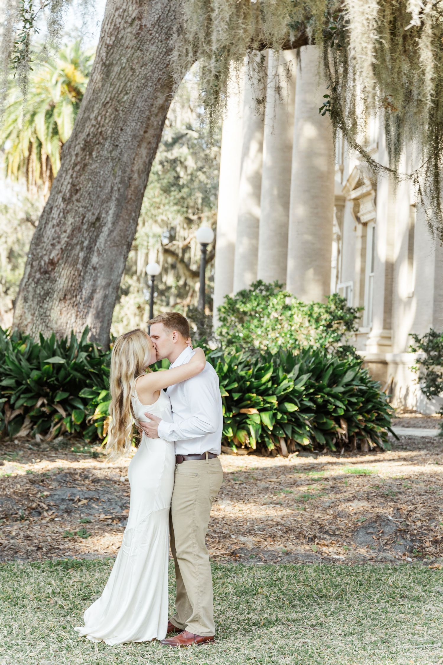 Elegant wedding portrait with couple embracing among Spanish moss and classical architecture.