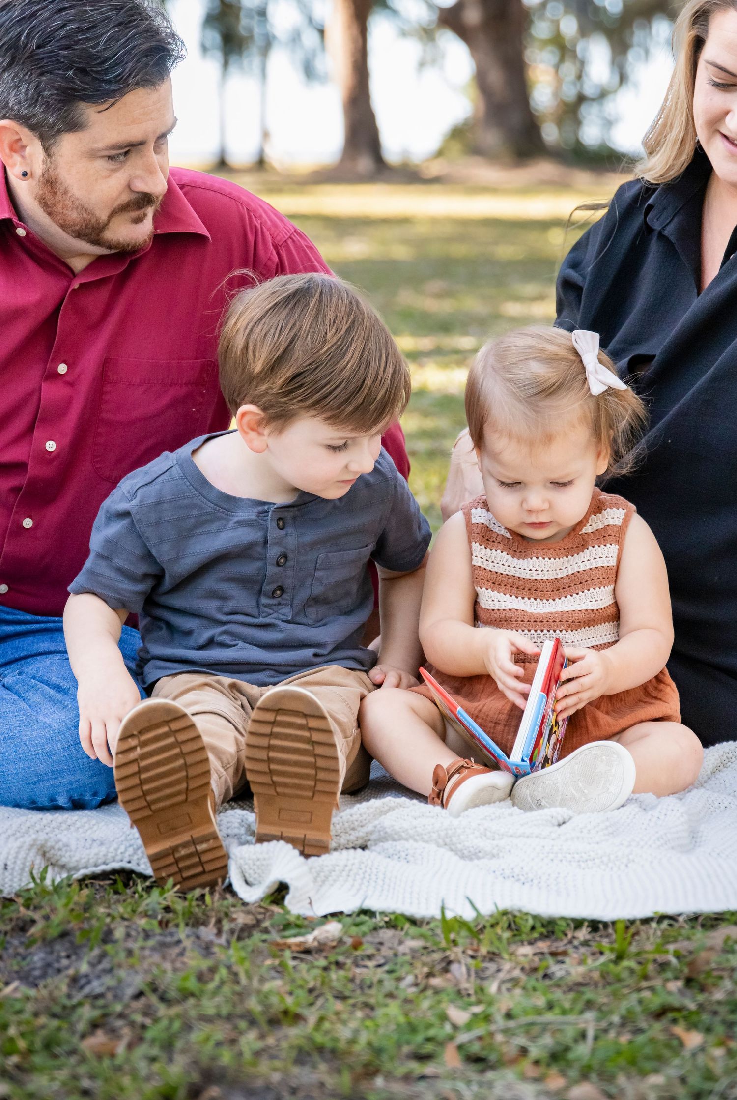 Family sitting together on blanket outdoors sharing intimate moment.