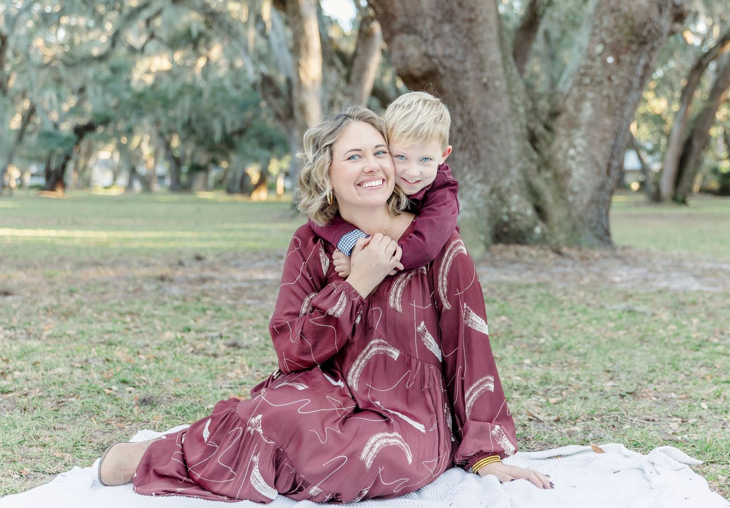 A joyful embrace between parent and child sitting on a white blanket outdoors.