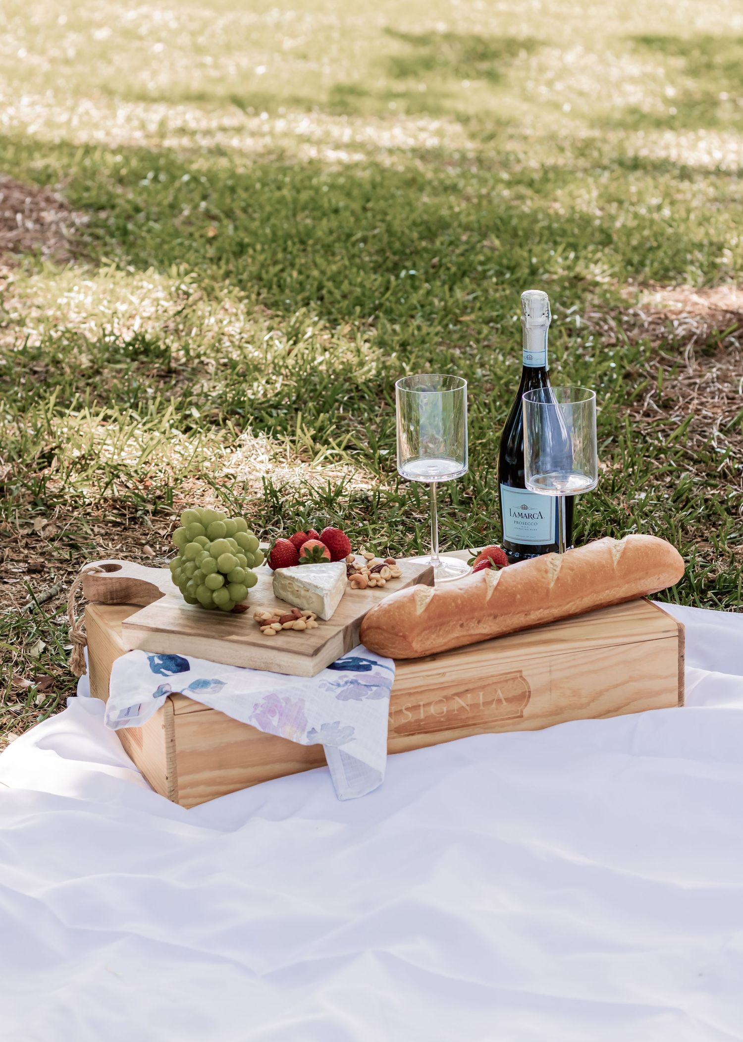 Elegant picnic setup with wine, fresh bread, and snacks on wooden serving boards outdoors.