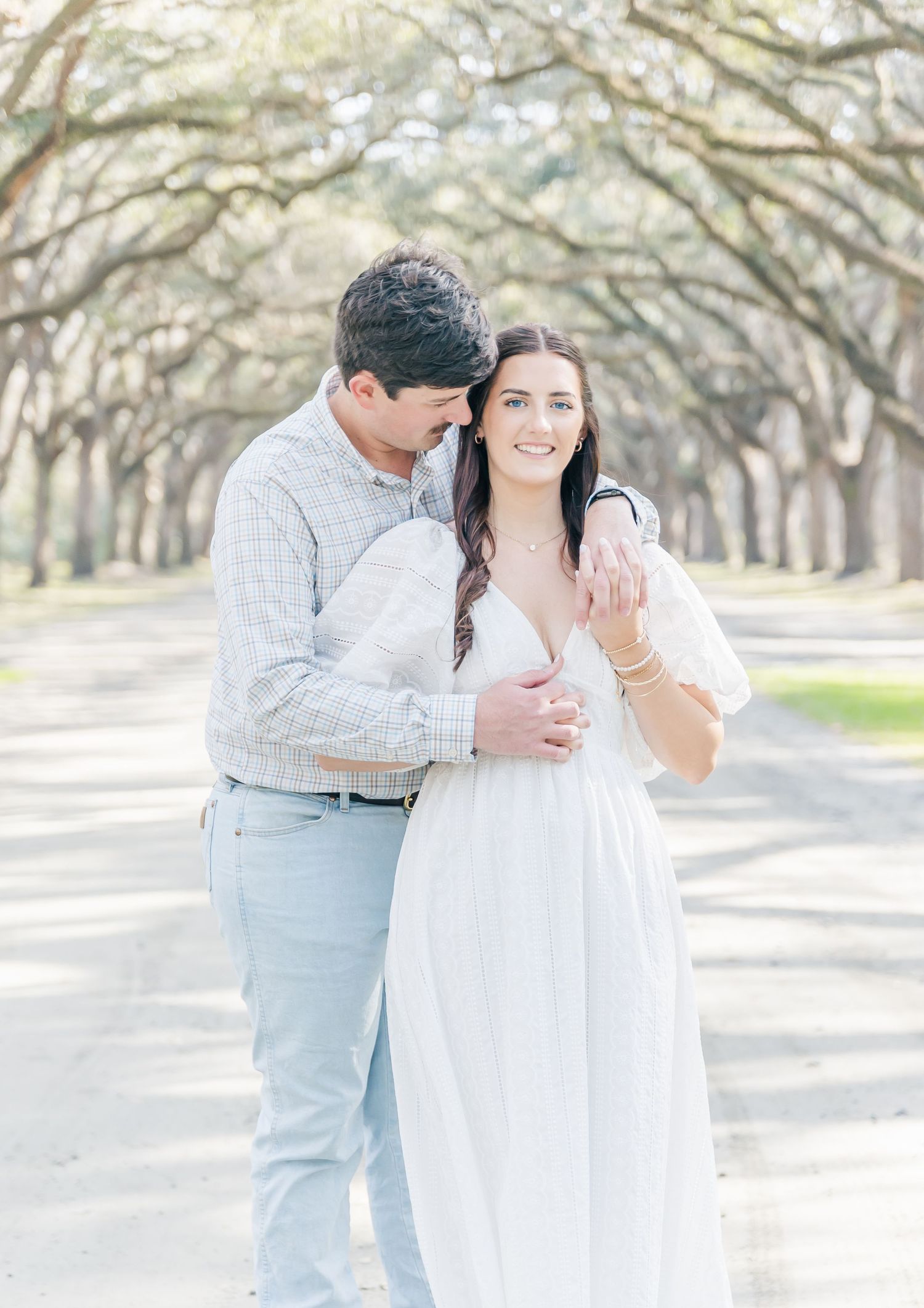 A joyful couple shares laughter and embraces under a natural cathedral of oak branches.
