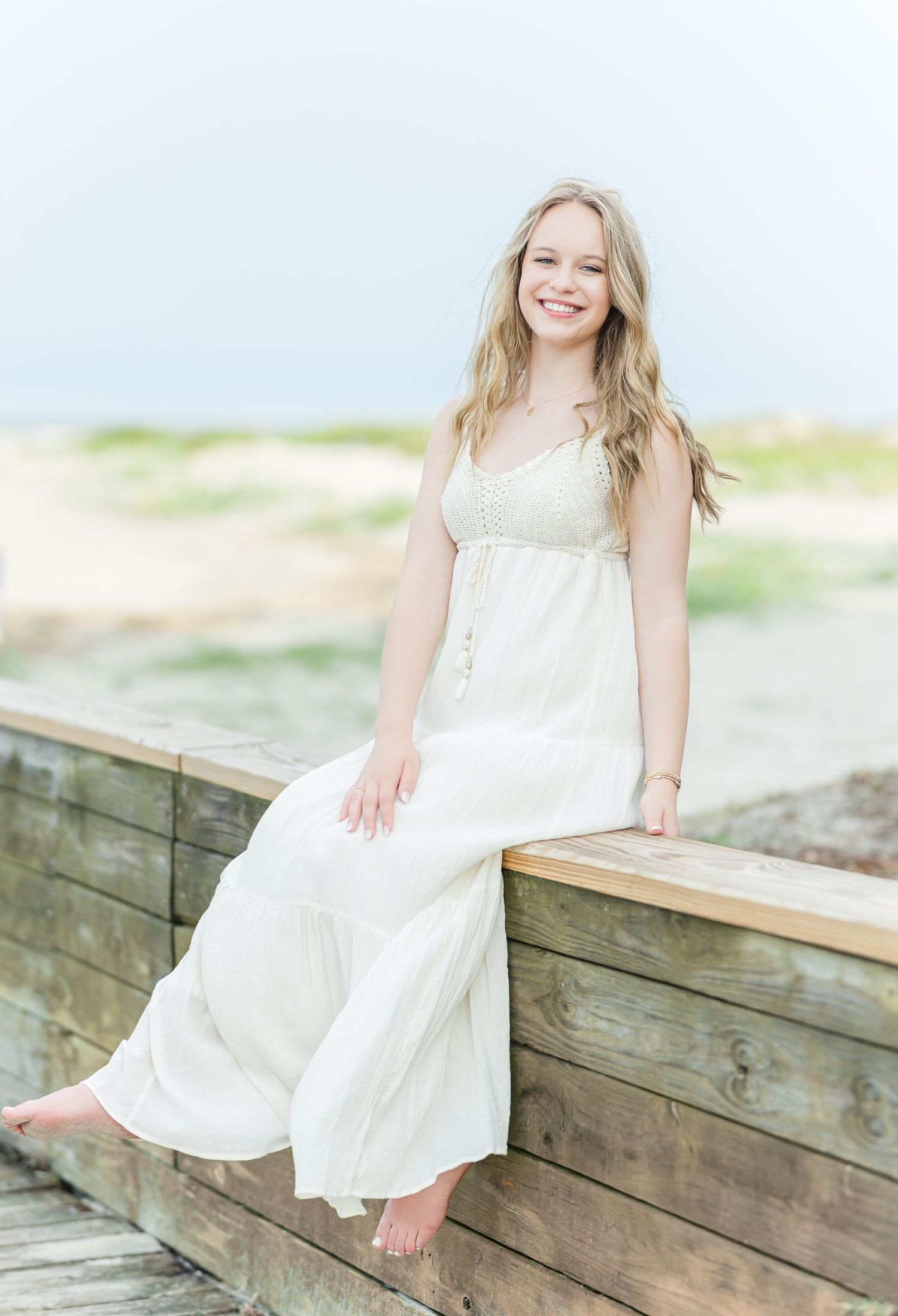 Casual beach portraits on weathered wooden boardwalk wearing a breezy white summer dress.