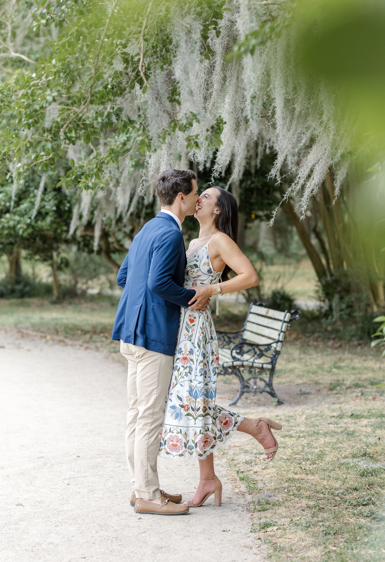 Couple sharing a romantic kiss on a garden path surrounded by lush trees draped with Spanish moss.