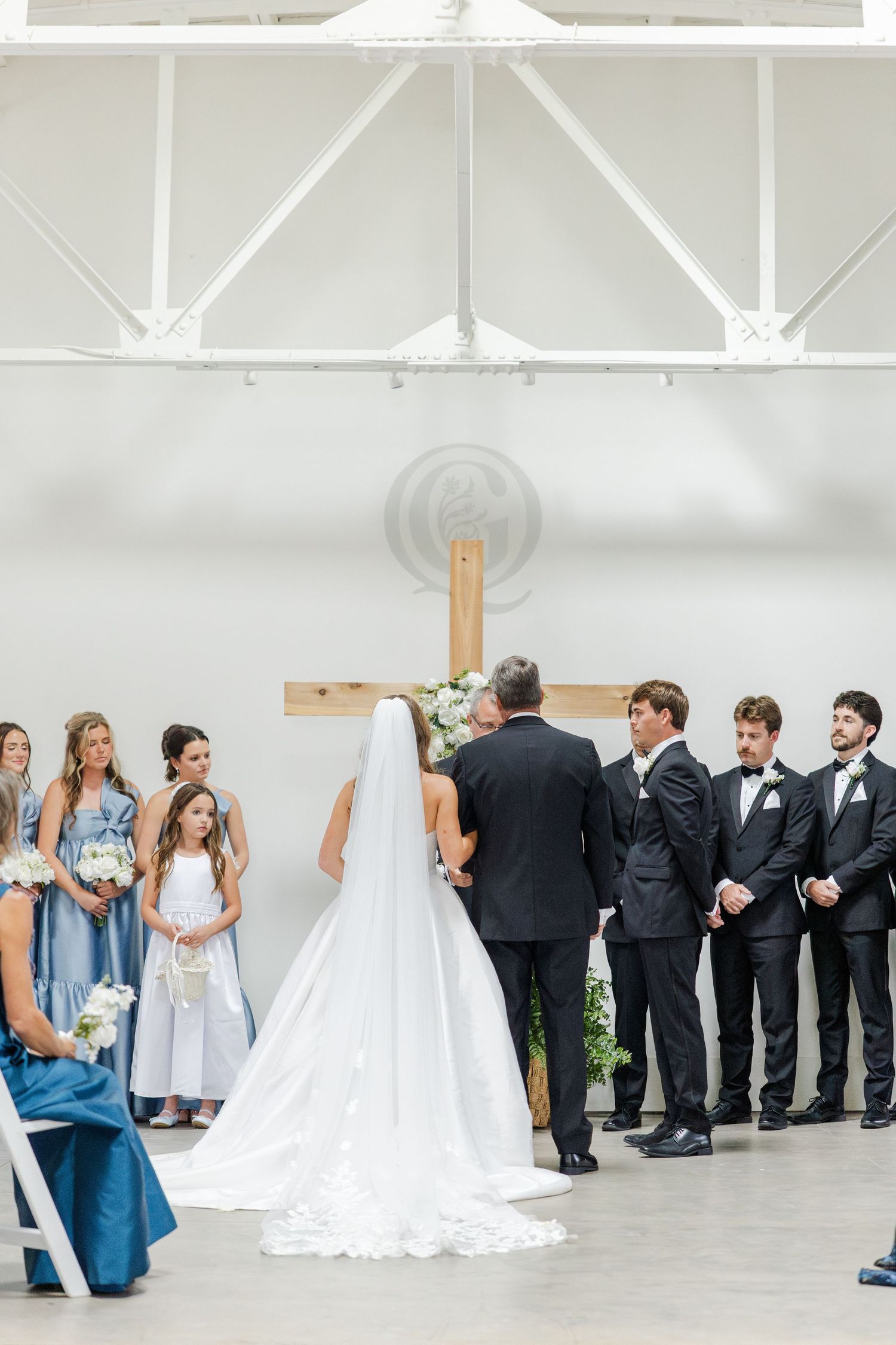 Bride with cathedral veil at altar with wedding party during indoor church ceremony.