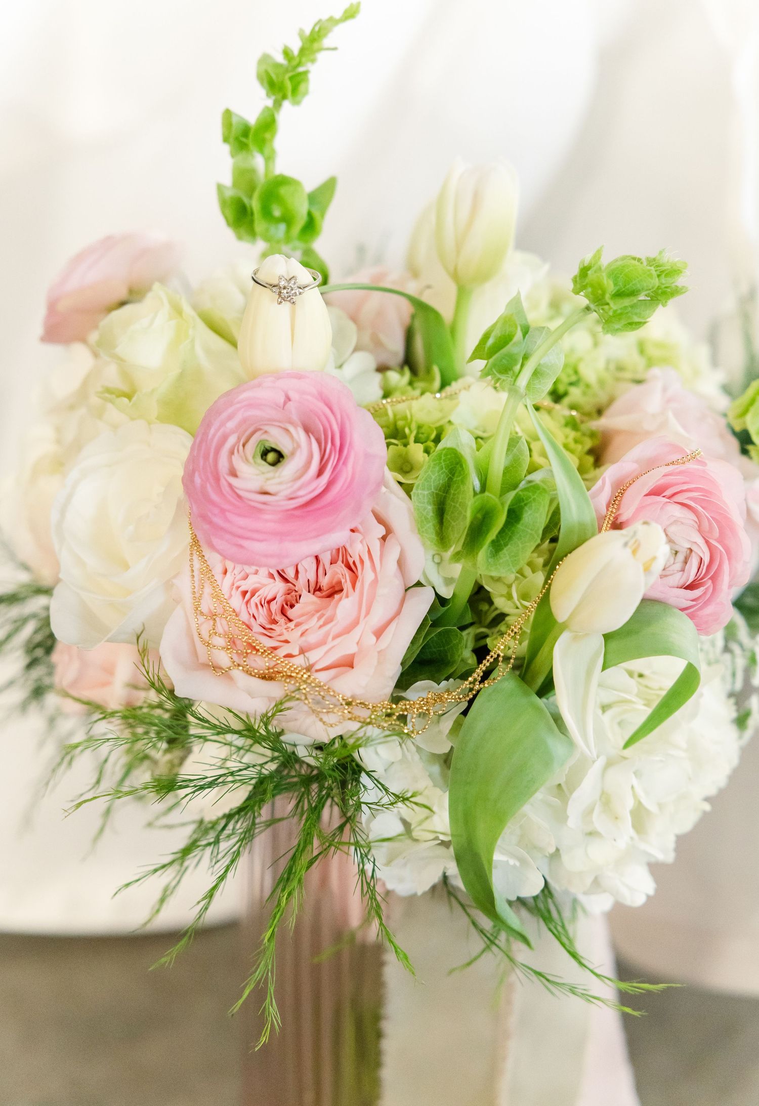 Romantic bridal bouquet featuring pink ranunculus, garden roses, white tulips, and greenery.